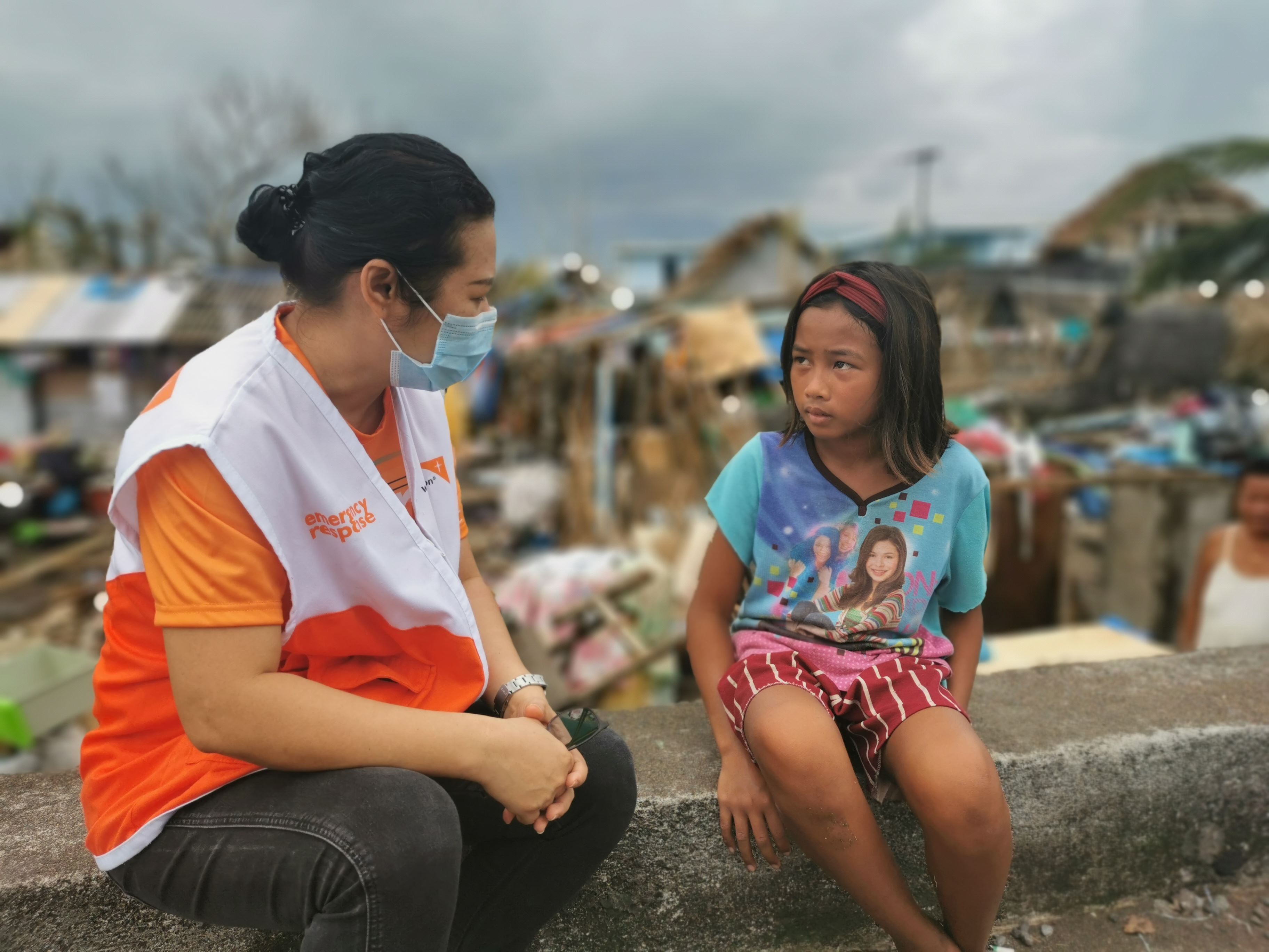 Un voluntario de World Vision con mascarilla habla con una niña de Filipinas
