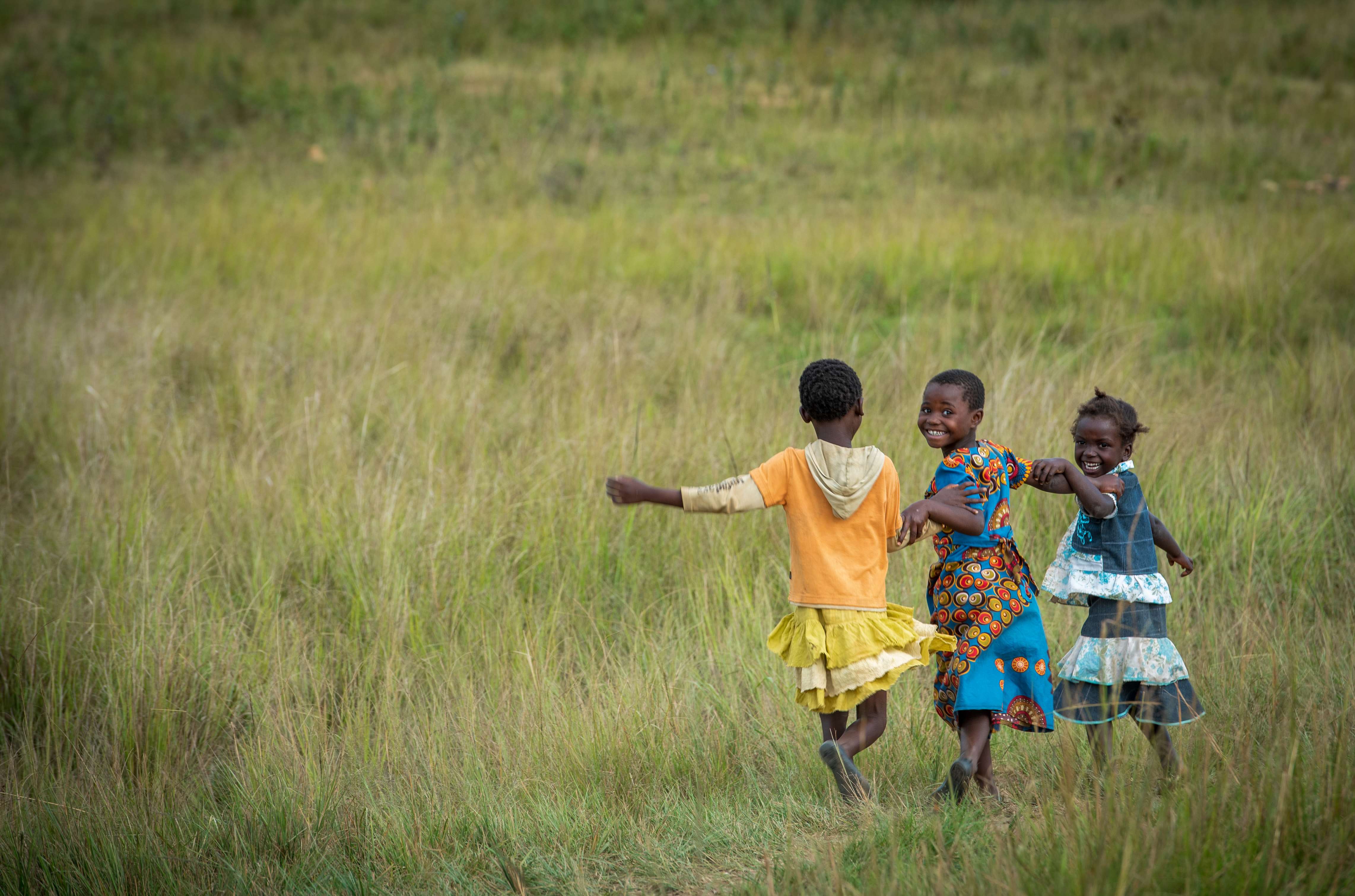 Tres niños corren felices por un campo en Zambia