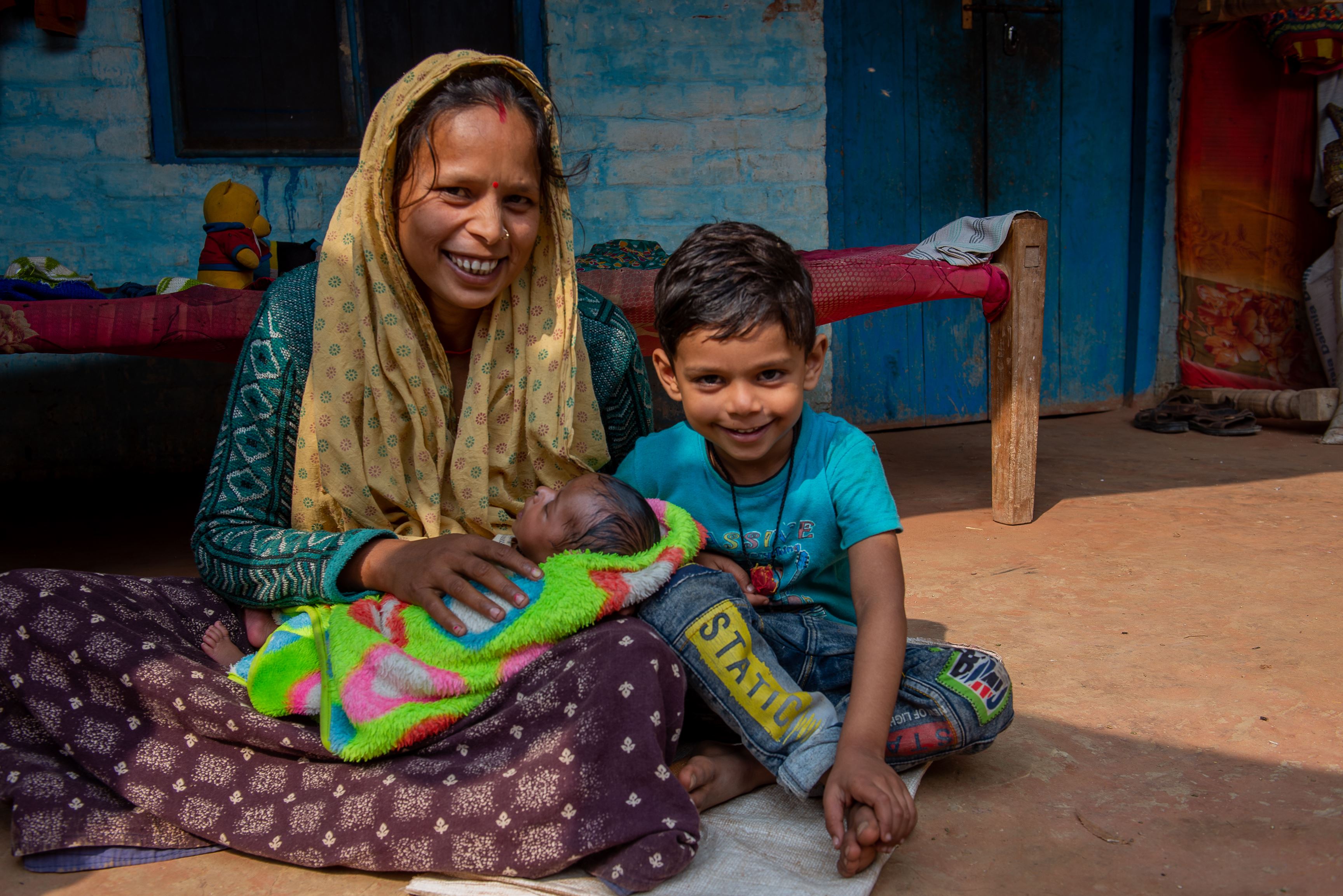 Madre de la India y su hijo sentados en el suelo de su casa y sonriendo a la cámara