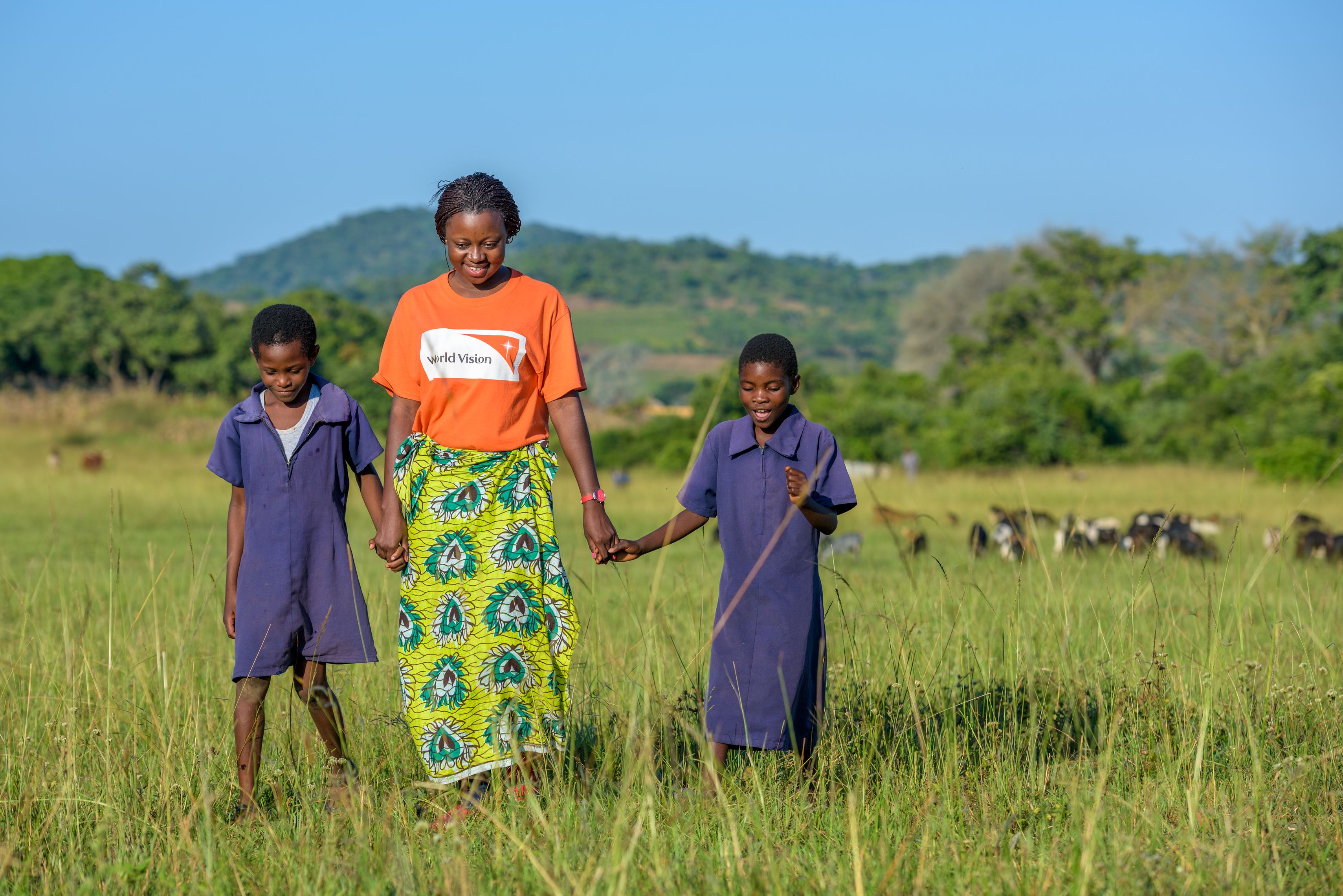 Dos niñas  andan por un prado de la mano de una miembro del personal de World Vision