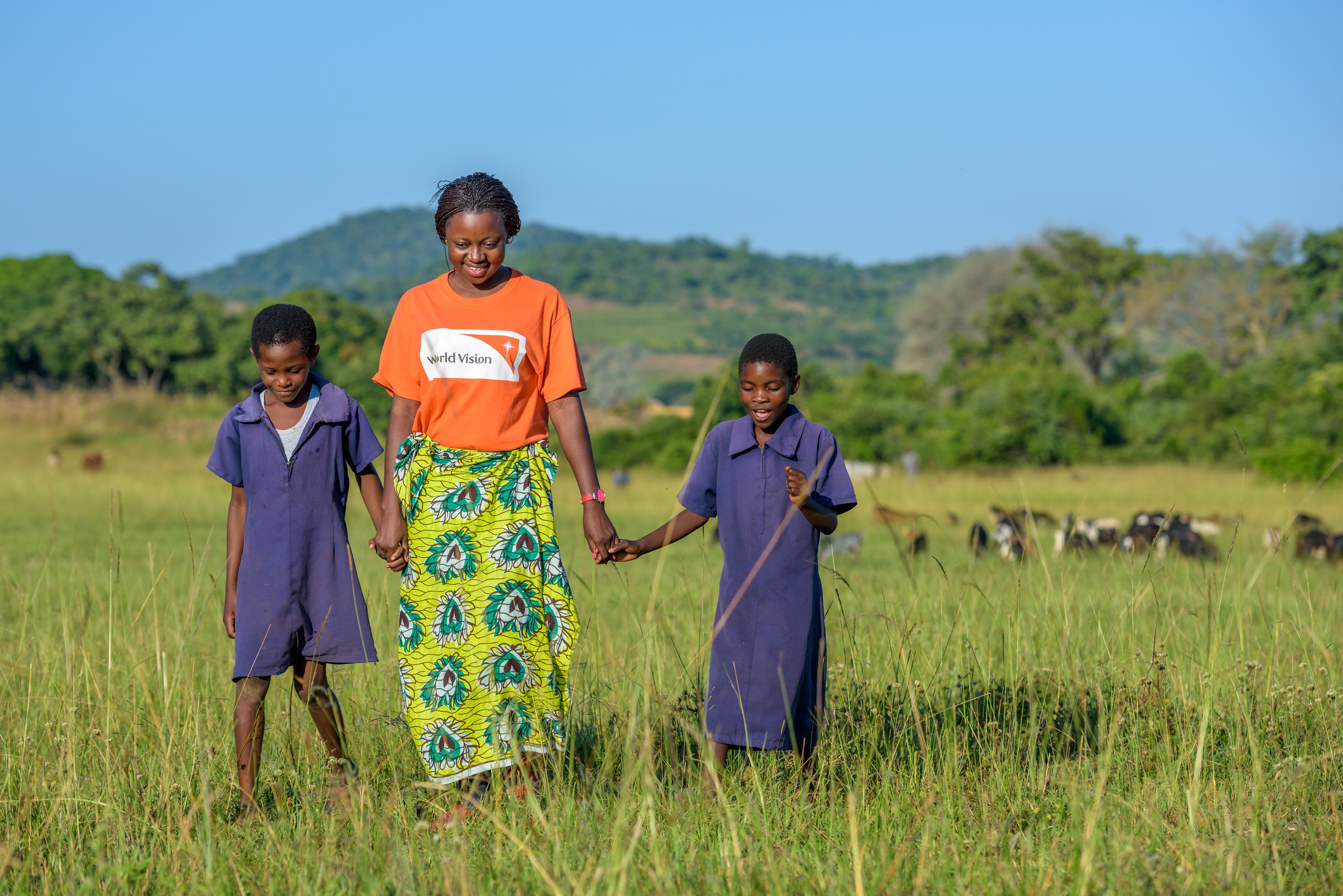 Un miembro del personal de World Vision Zambia camino junto con dos niñas
