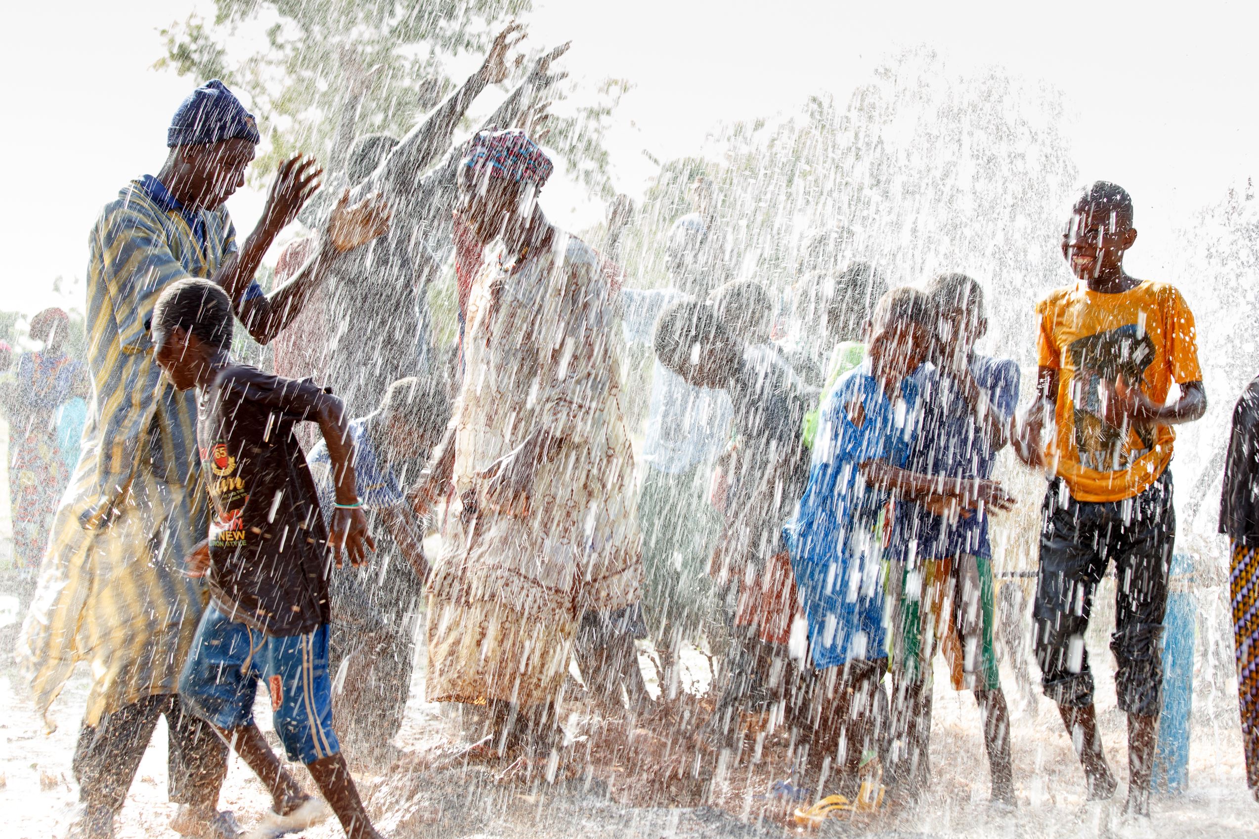 Una comunidad en Mali bailando en el agua que fluye para celebrar el pozo número 150.000 de World Vision en el país
