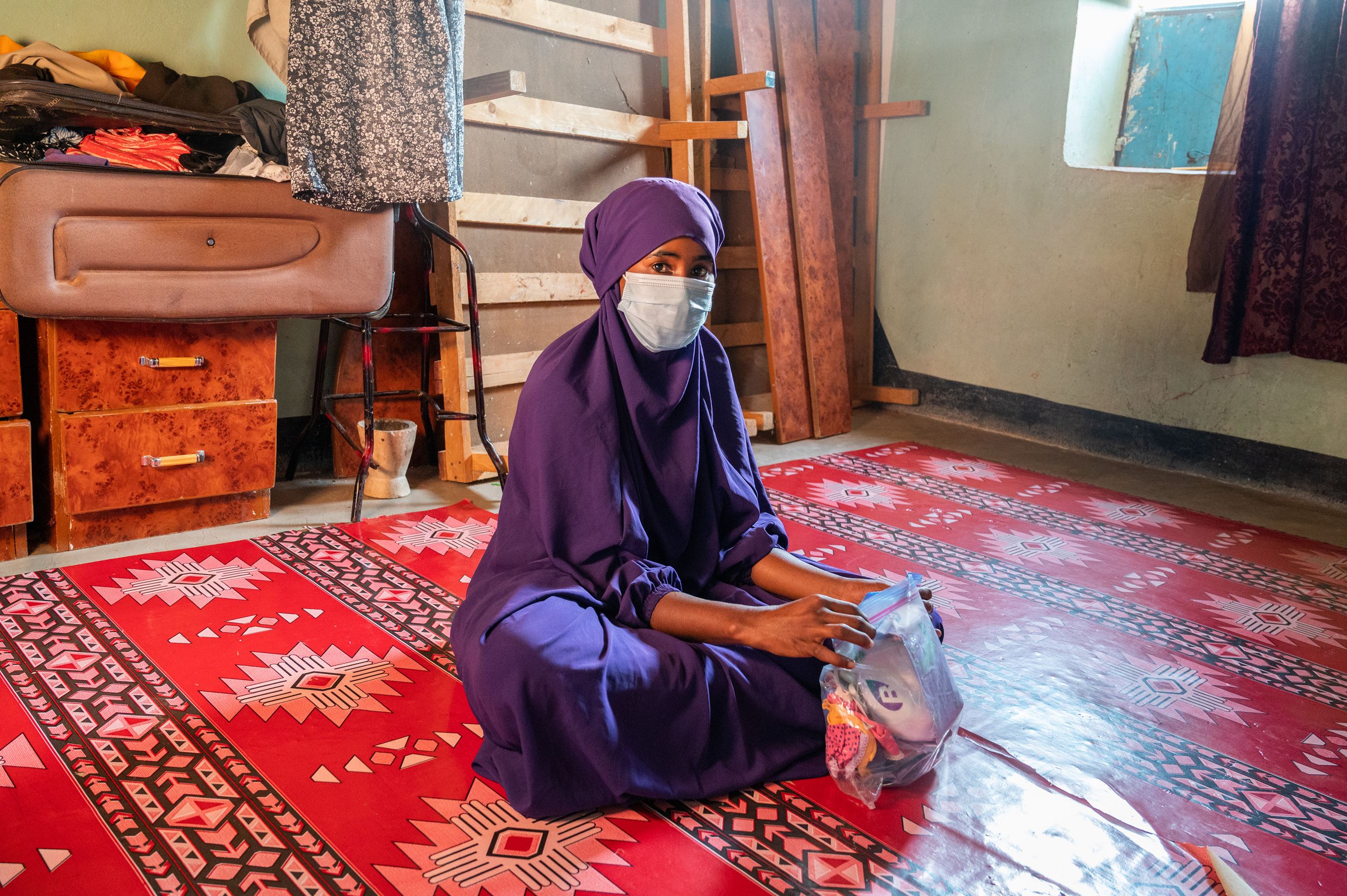 Niña de Somalia con hijab y mascarilla, sentada en el suelo de su casa mientras sostiene en sus manos el paquete de higiene donado por World Vision.