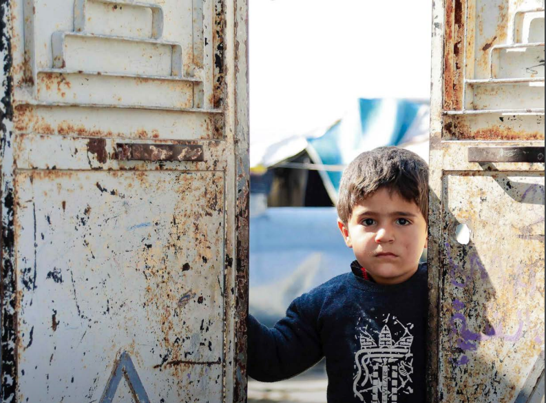 Niño sirio mirando con tristeza a través de una puerta vieja