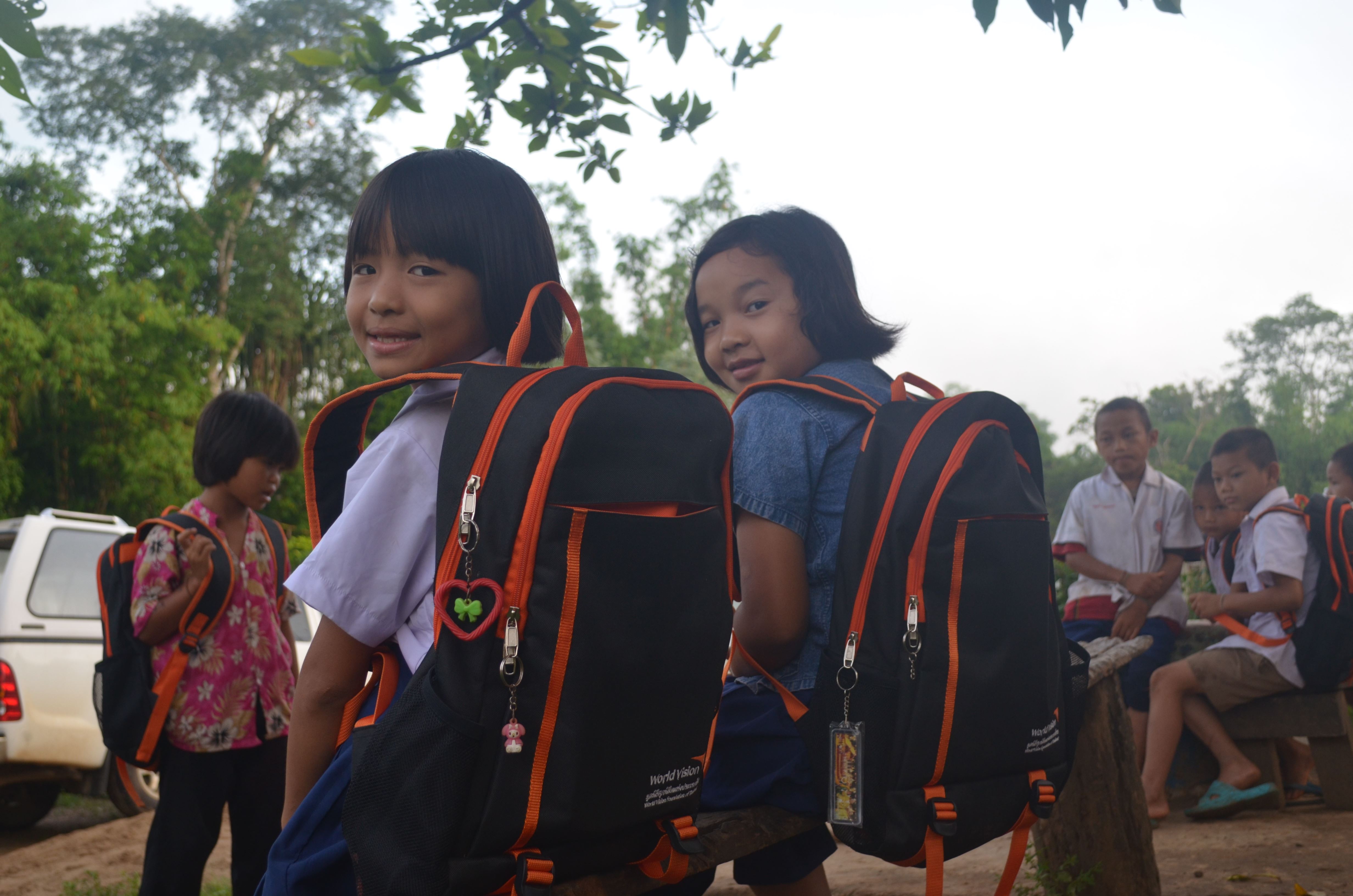 Escolares tailandesas sonríen mostrando sus mochilas escolares, donadas por los patrocinadores de World Vision.