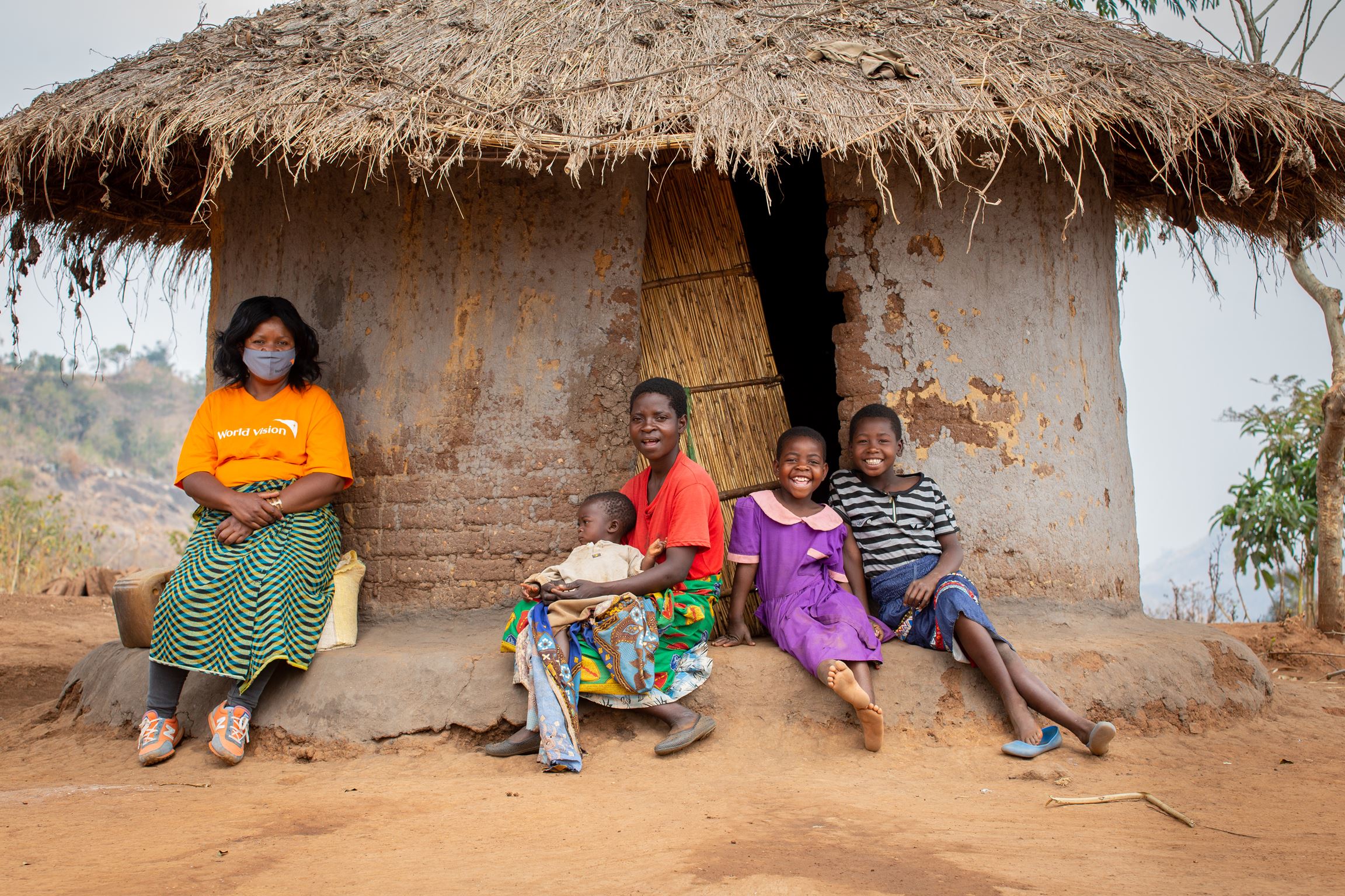 Una familia de cuatro miembros de Malawi sentada delante de su casa