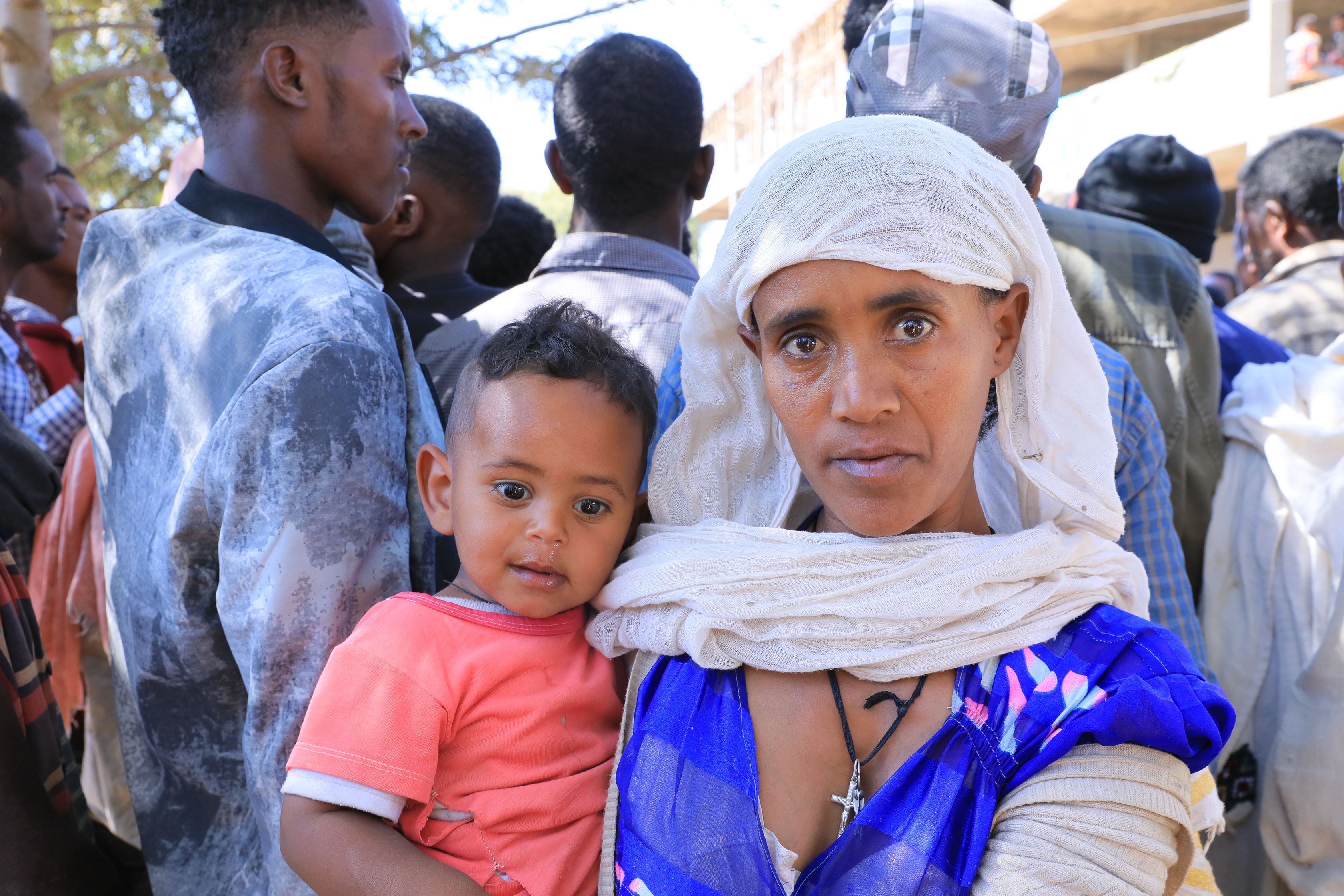 Madre en Etiopia con su hijo en brazos, al fondo un grupo de personas