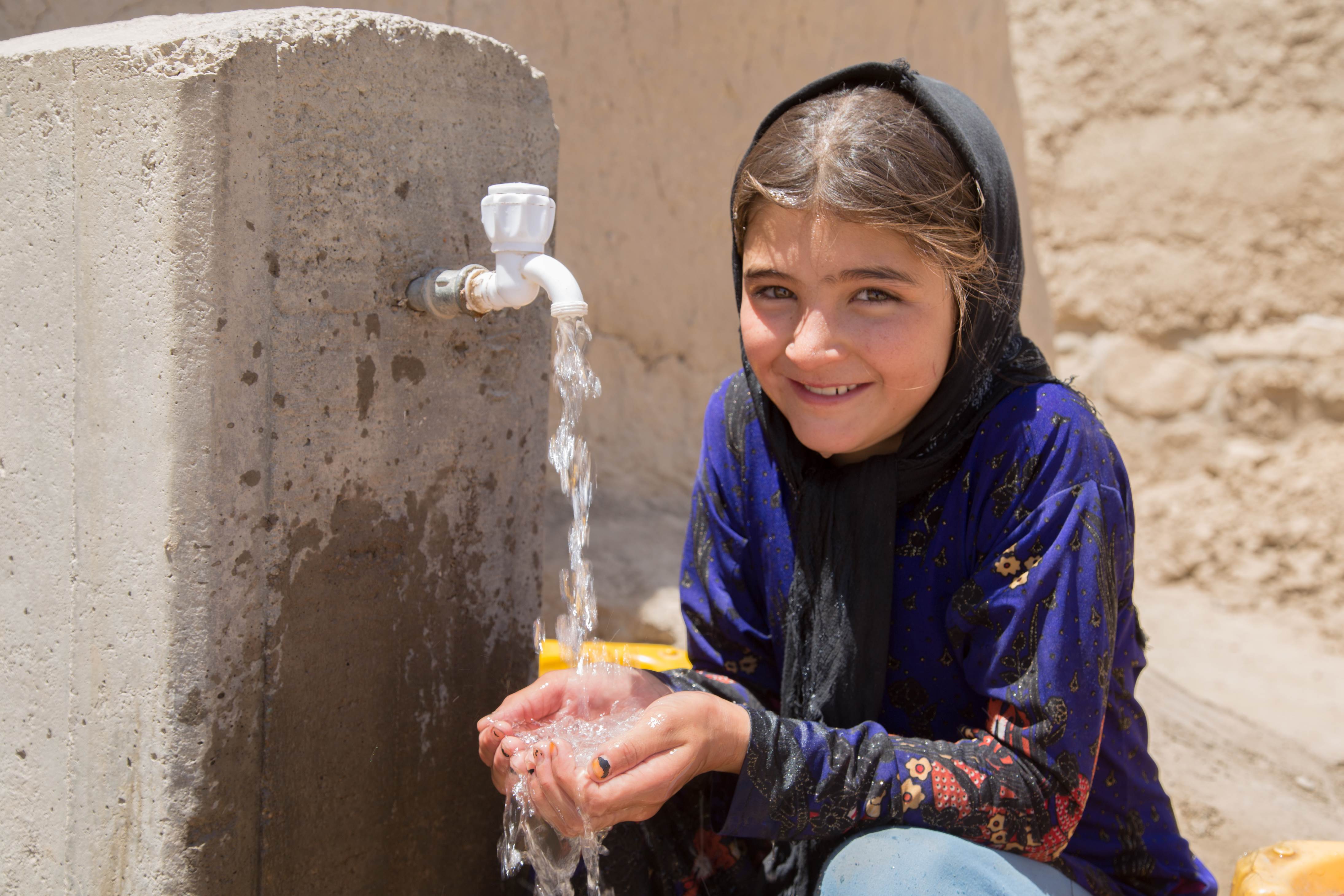 Niña afgana sonríe mientras se lava las manos en agua limpia de una fuente de agua filtrada y alimentada por energía solar establecida por World Vision