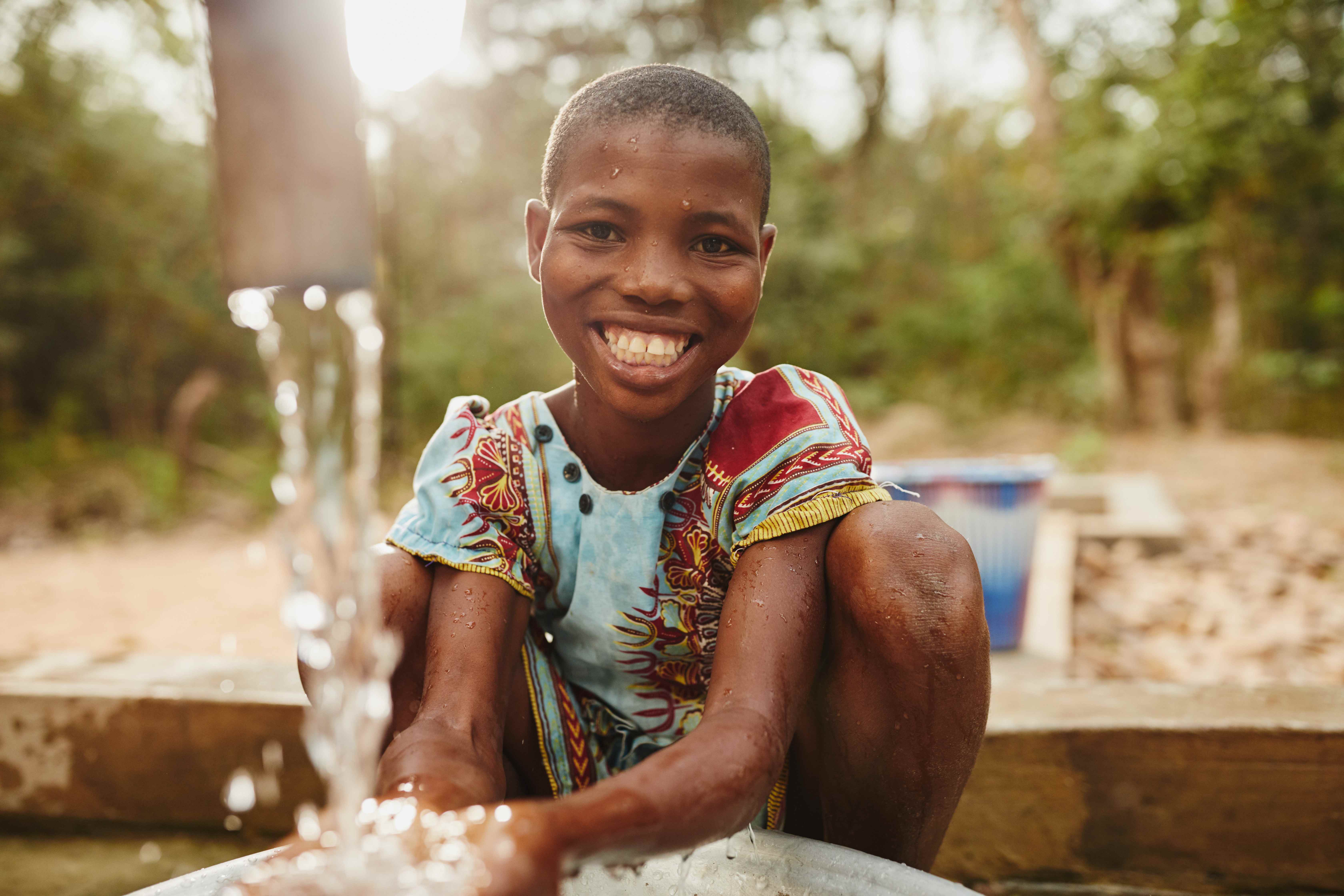 Niño cogiendo agua limpia de una tubería con sus manos, feliz mirando a la cámara