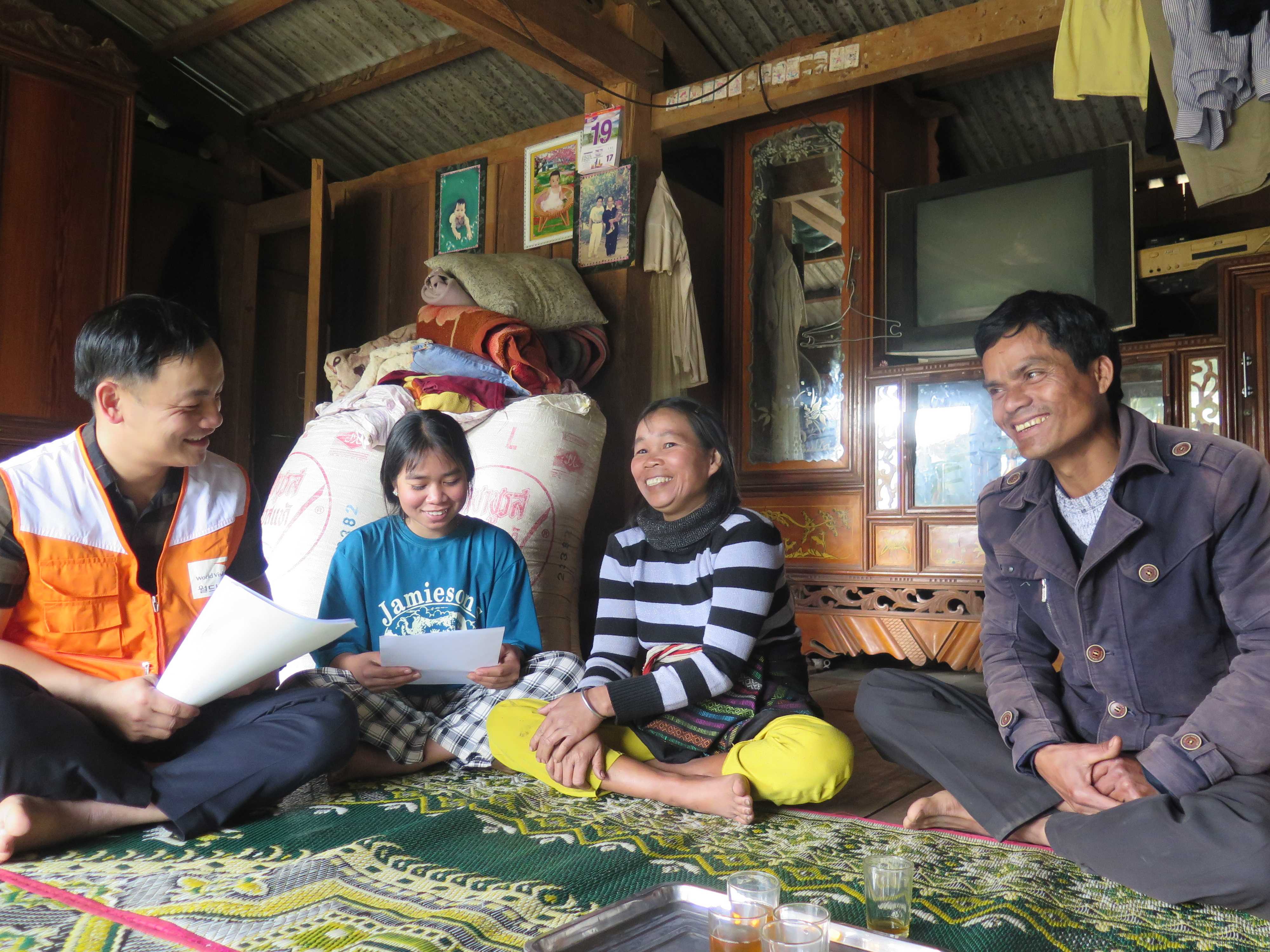 Una familia vietnamita de tres miembros sentada alrededor de una mesa y charlando con un voluntario de World Vision