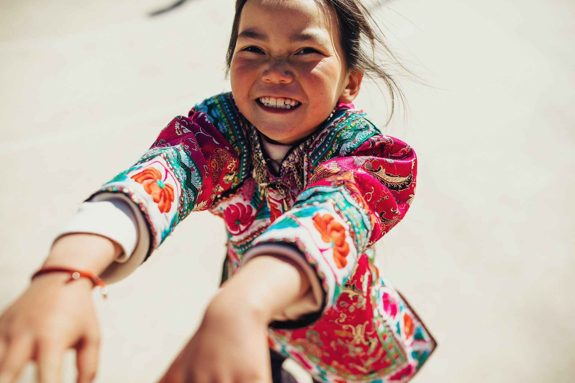 Niña de China con una colorida camiseta sonríe mientras extiende sus brazos a la persona que sostiene la cámara