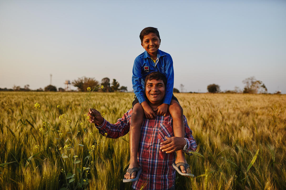Un padre lleva a su hijo sobre los hombros en un campo de la India