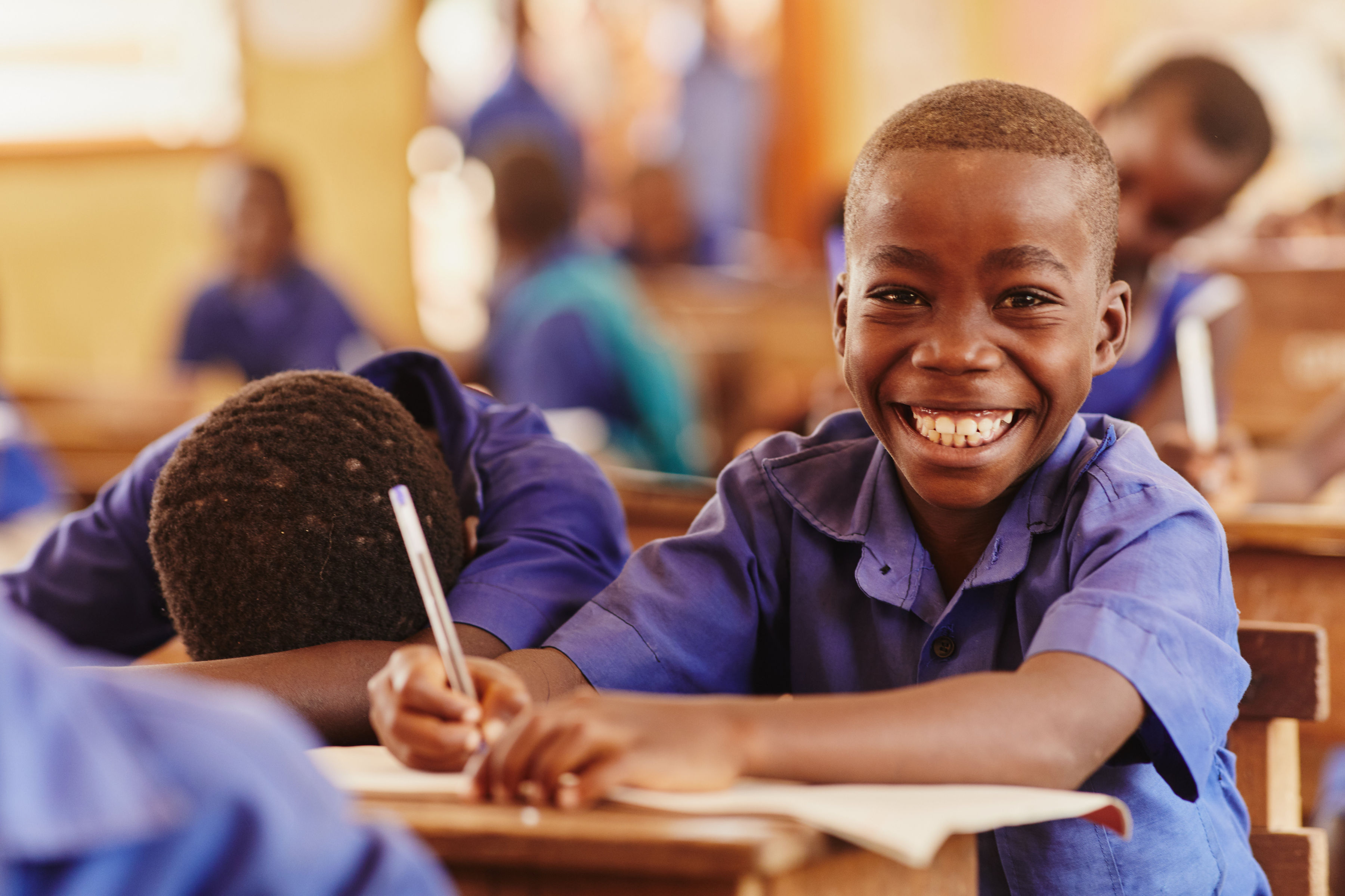 Niño de Ghana sonriendo y mirando a la cámara mientras está sentado en su pupitre con el uniforme escolar.