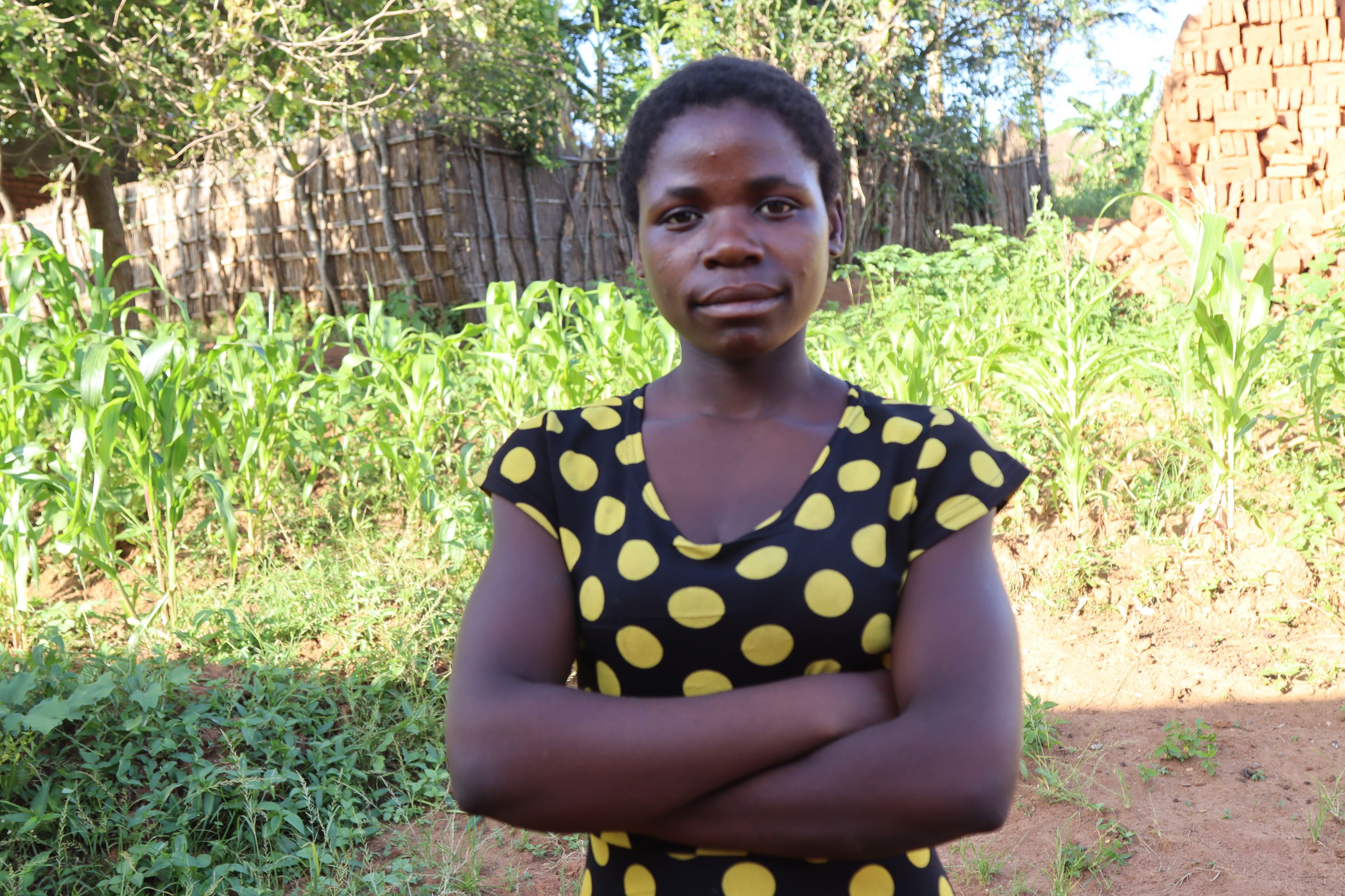 Niña de Malawi de pie con los brazos cruzados en un campo, mirando a la cámara