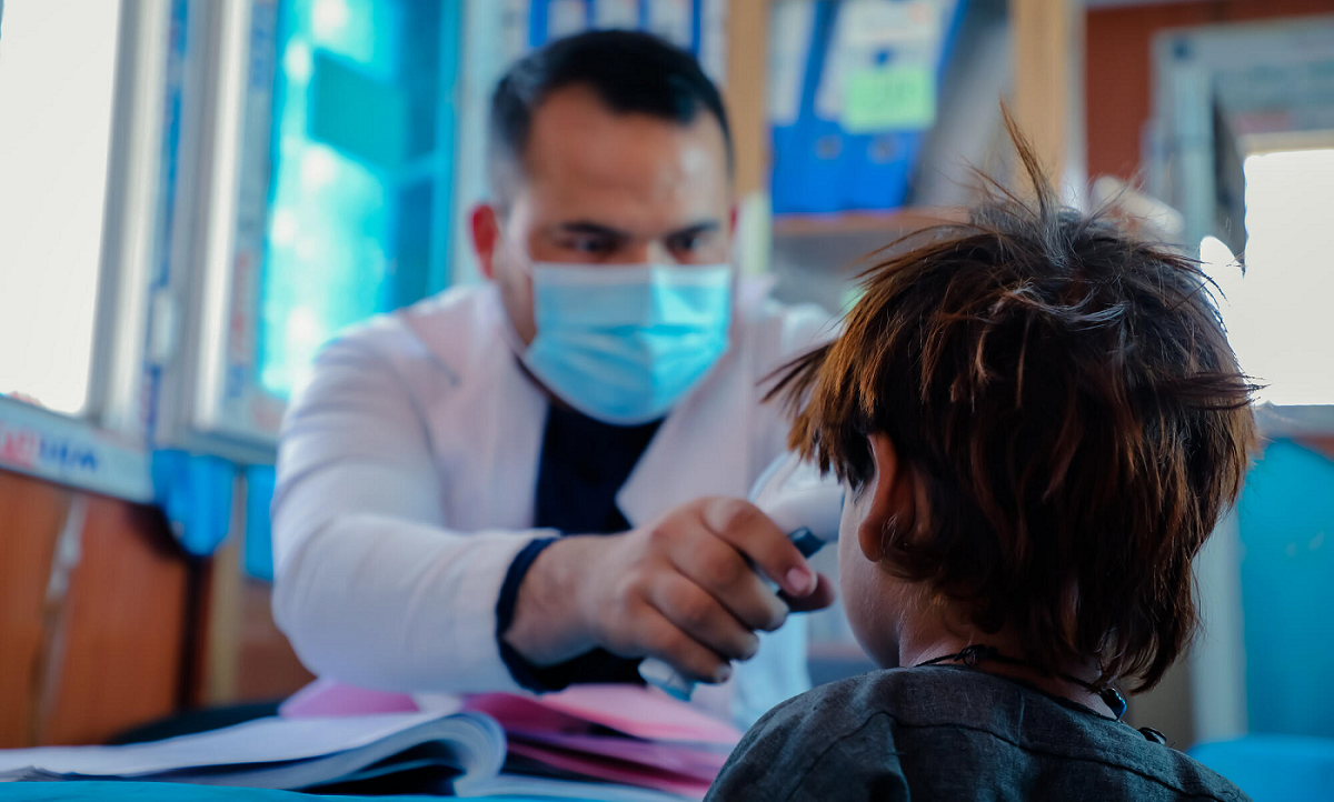 Un médico afgano con mascarilla comprueba la temperatura de un niño con un termómetro en la frente