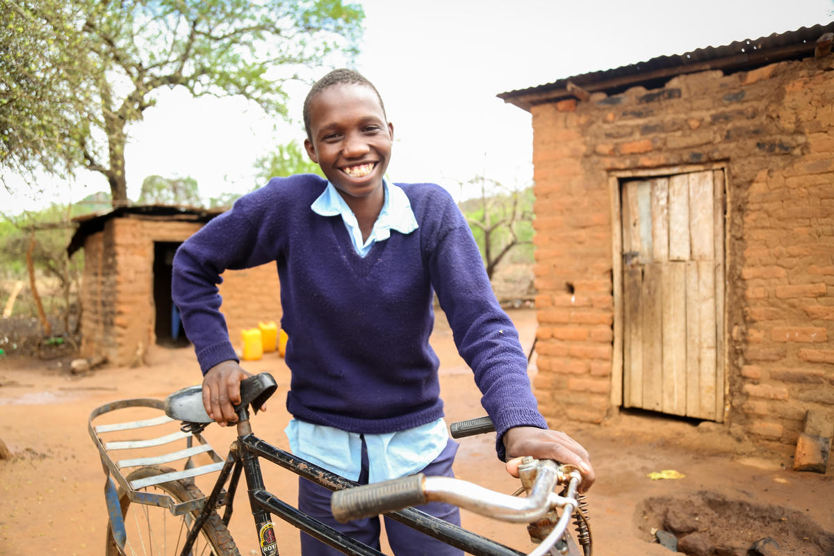 Niño sonriente en Kenia está al aire libre con su bicicleta