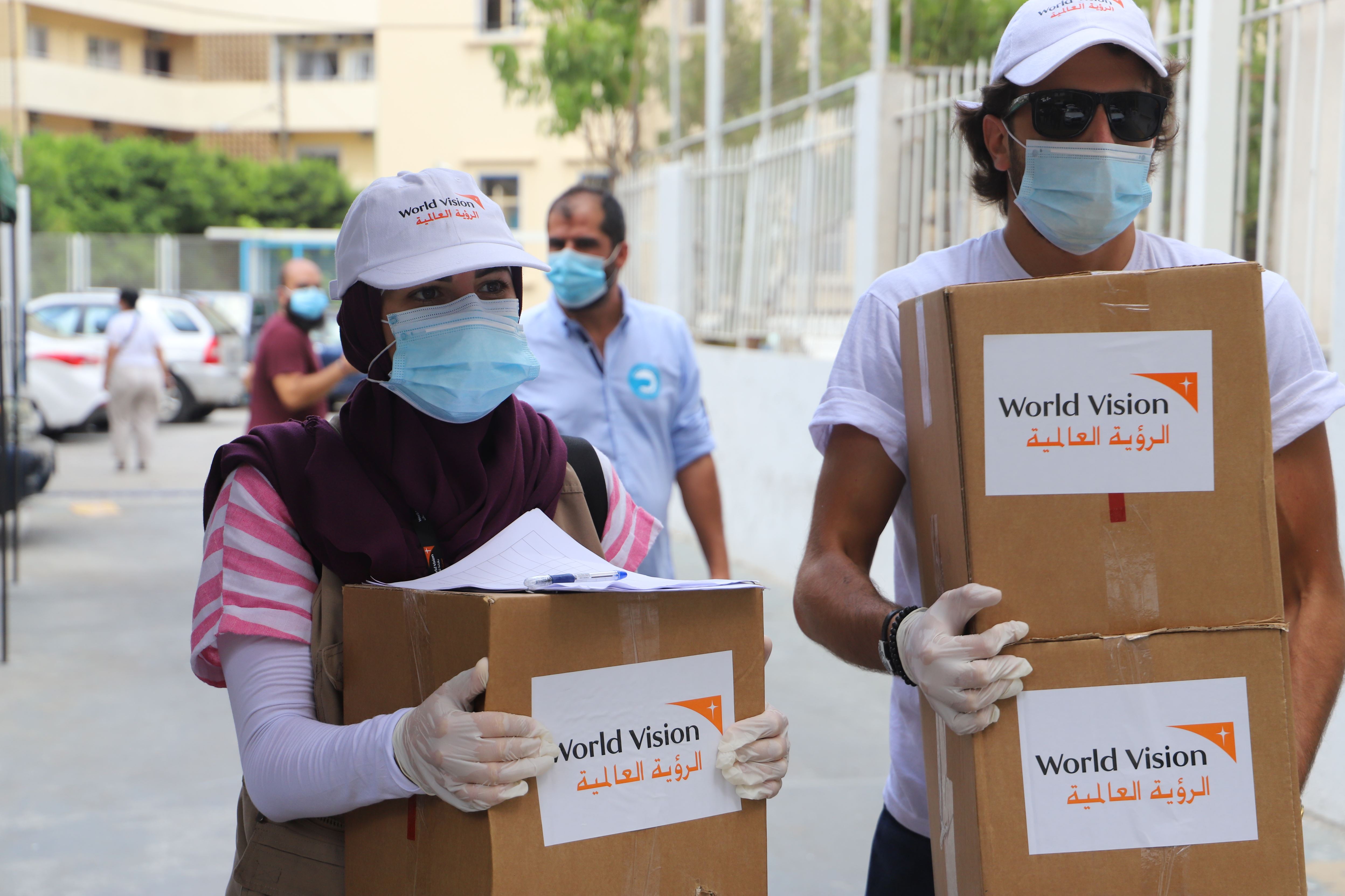 Miembros de World Vision usando mascarillas y guantes llevan cajas para distribuir mini kits de alimentos