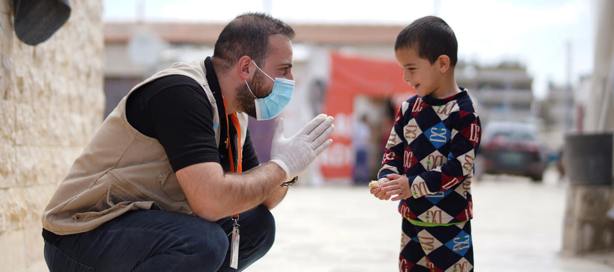 Un representante de World Vision con mascarilla hablando con un niño en un campo de refugiados de Jordania.