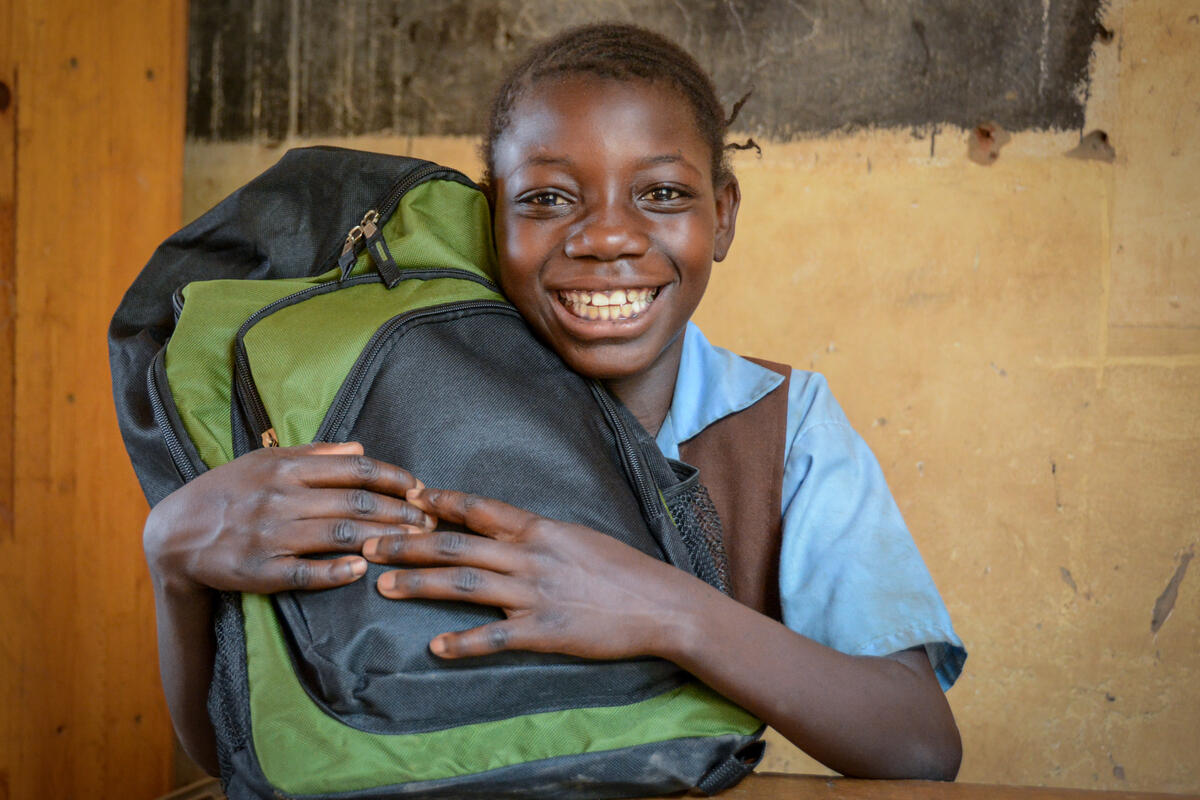 Niña de Zambia sonríe a la cámara sosteniendo su mochila escolar en sus brazos
