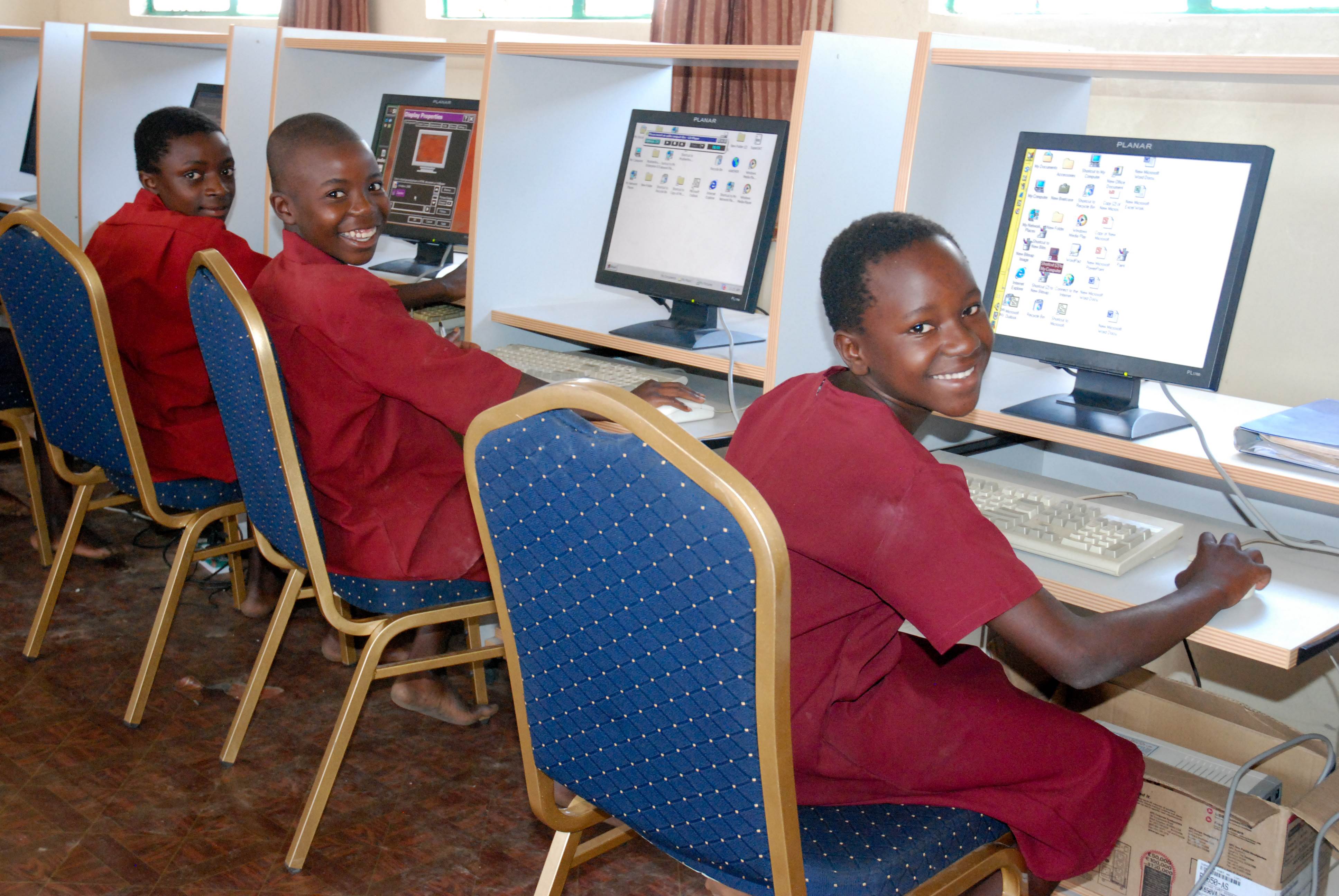 Tres niños en uniforme rojo, cada uno frente a un ordenador