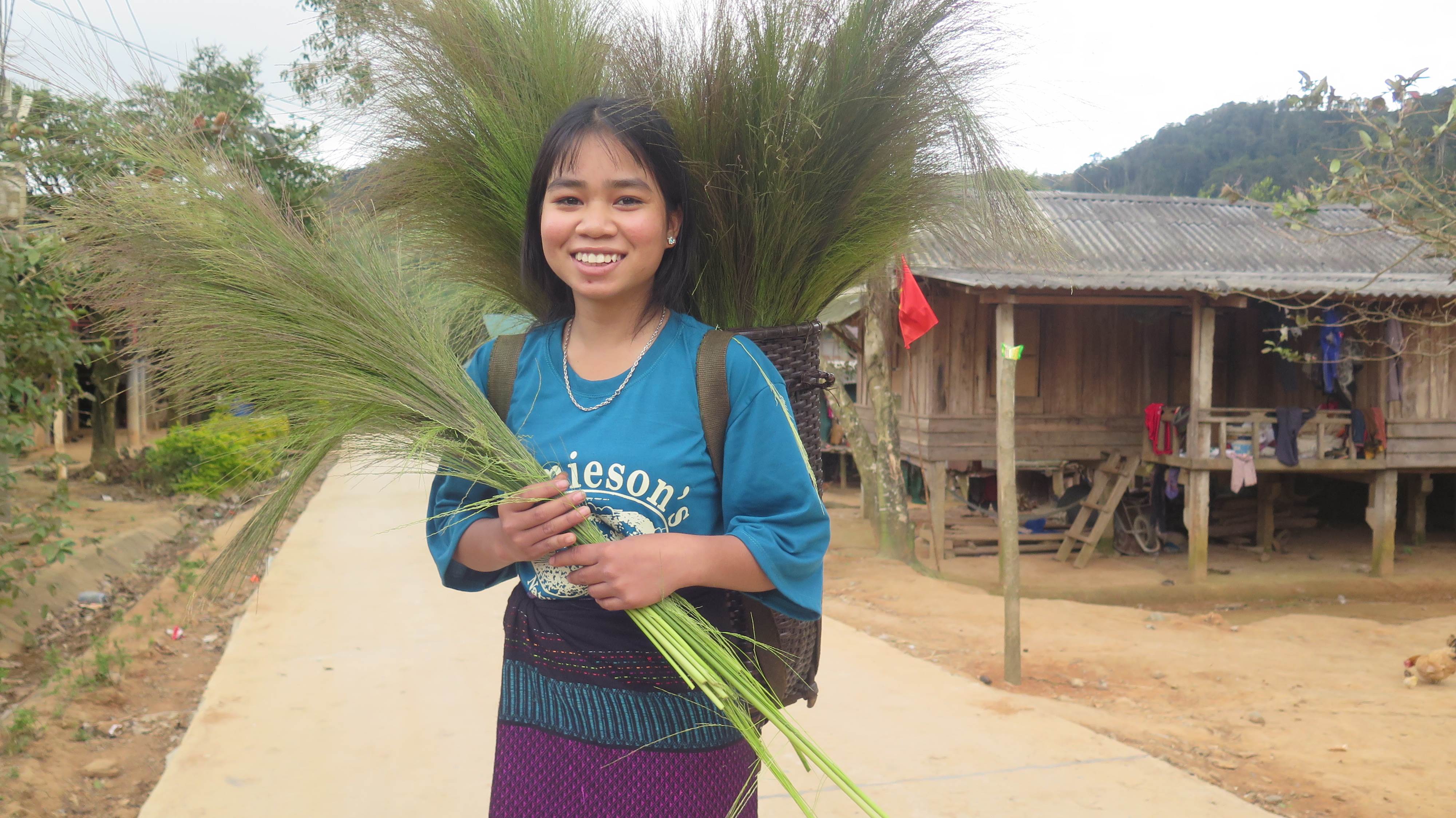 Niña de Vietnam sosteniendo unas ramas mientras sonríe y mira a la cámara