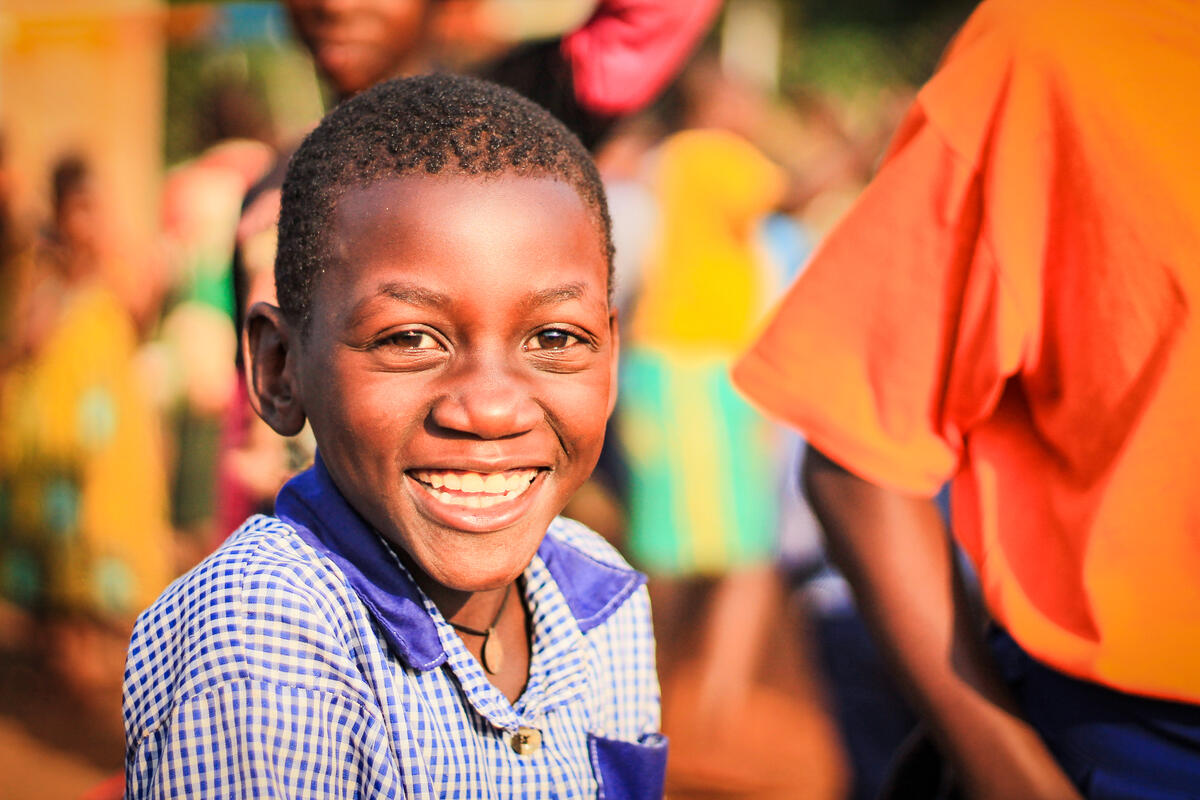 Niño ugandés sonríe, sentado afuera junto con otros niños en el fondo