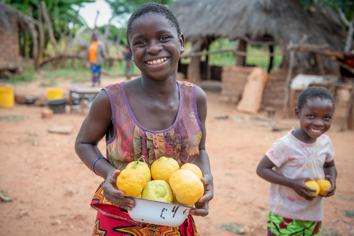 Niña y niño en Zambia sonríen, de pie afuera sosteniendo un montón de limones
