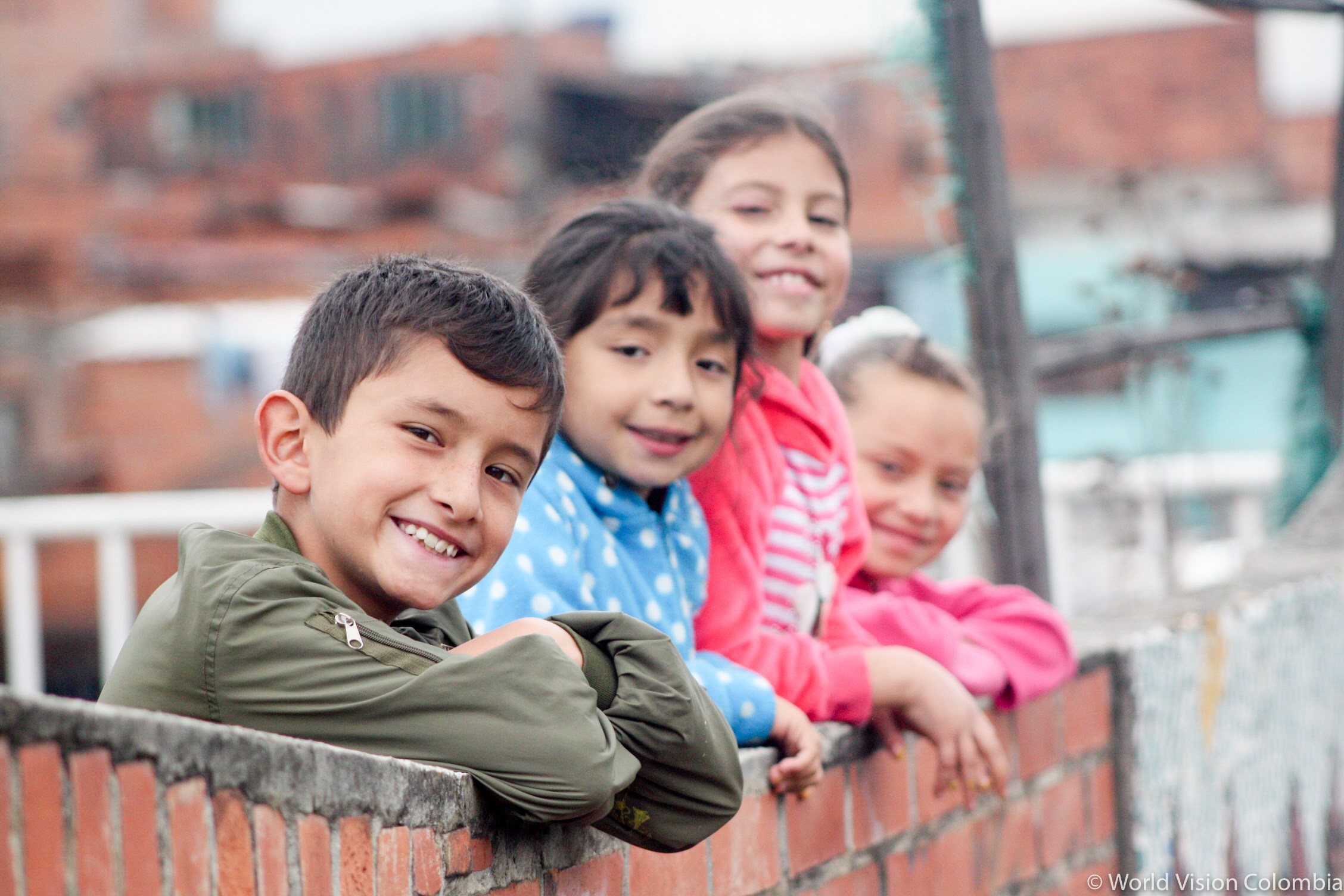Cuatro niños están apoyados en una pared, mientras sonríen y posan.