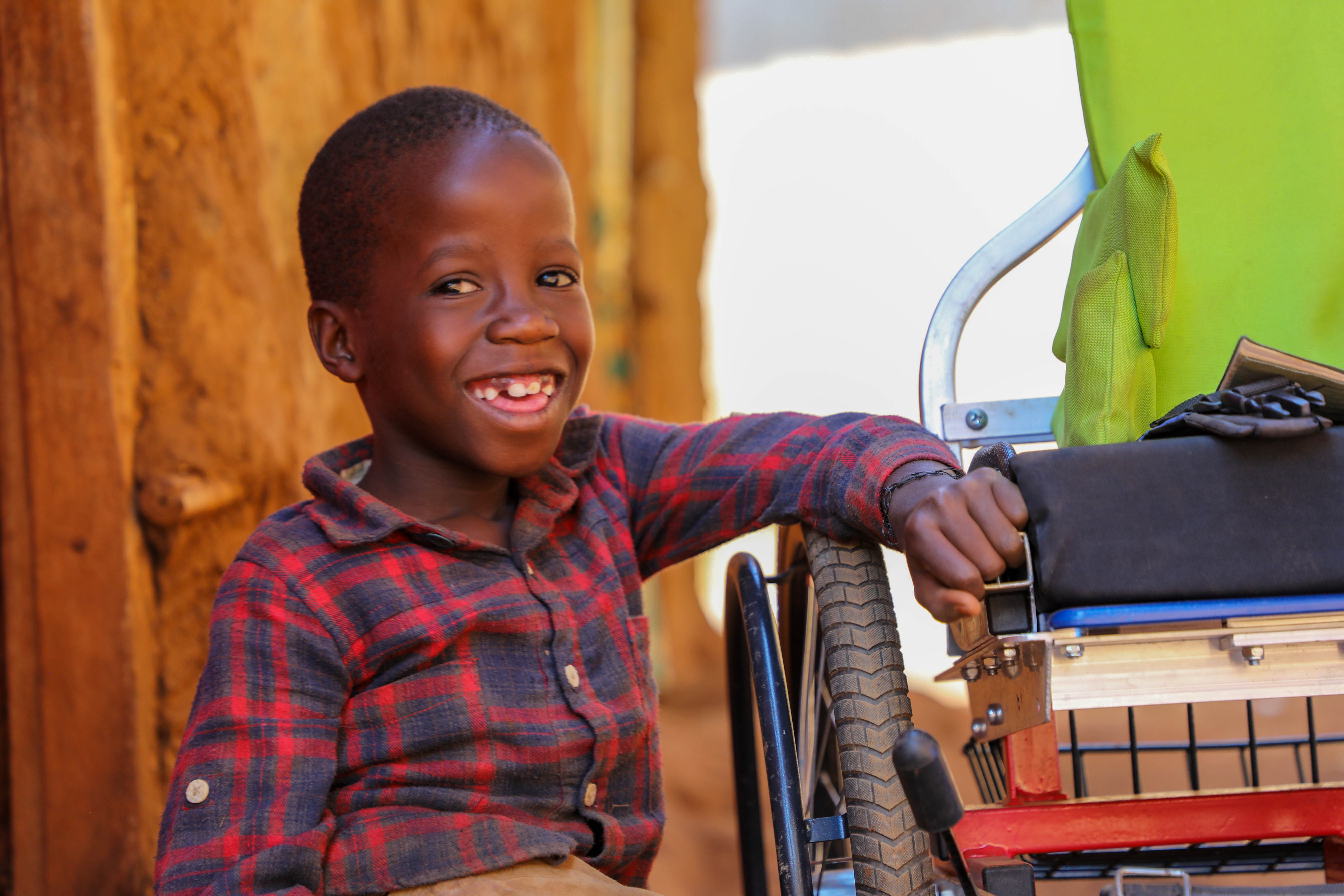 Un niño ugandés en silla de ruedas sonríe ampliamente a la cámara