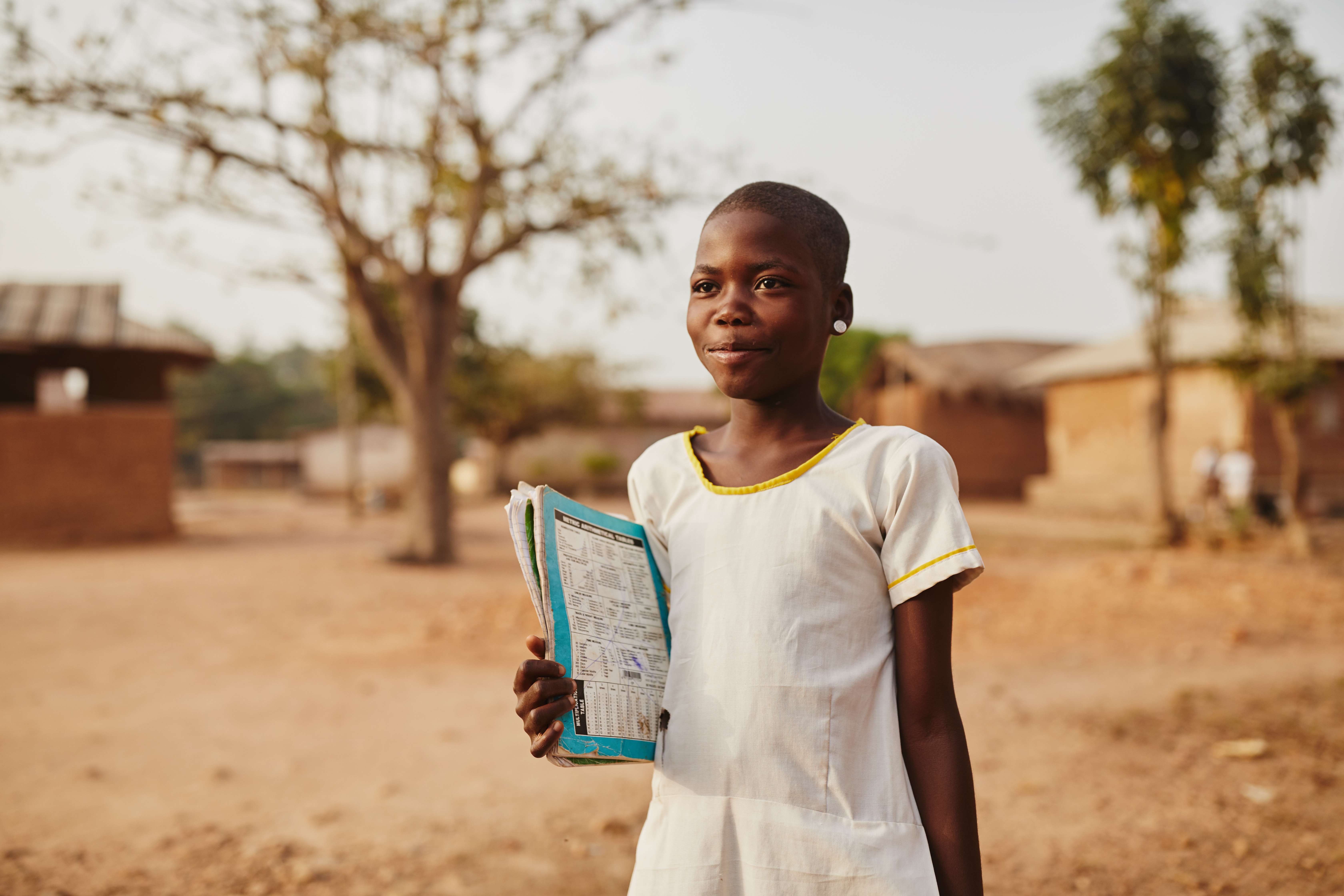 Niña de Ghana con vestido blanco mientras sostiene su certificado de nacimiento y mira a lo lejos
