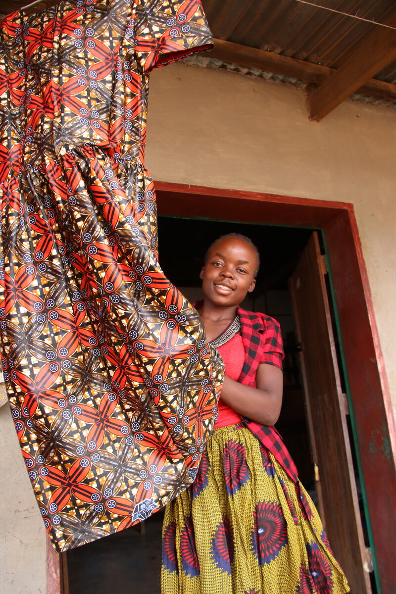 La niña apadrinada de 19 años, Mwila, muestra un vestido que cosió gracias al entrenamiento recibido