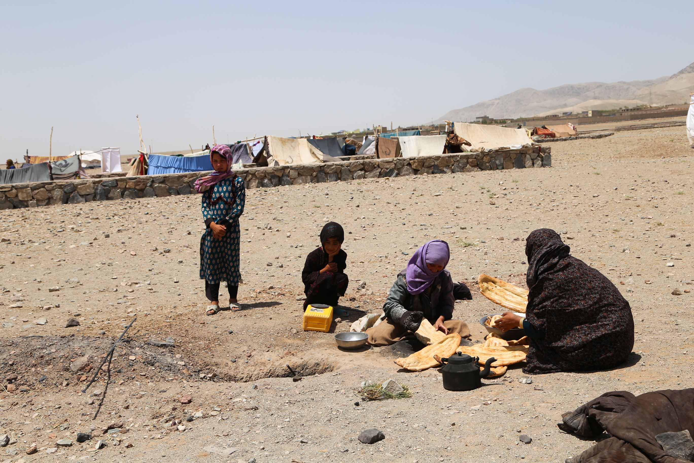Una familia afgana de cuatro miembros se sienta en el suelo al aire libre y comparte la comida.