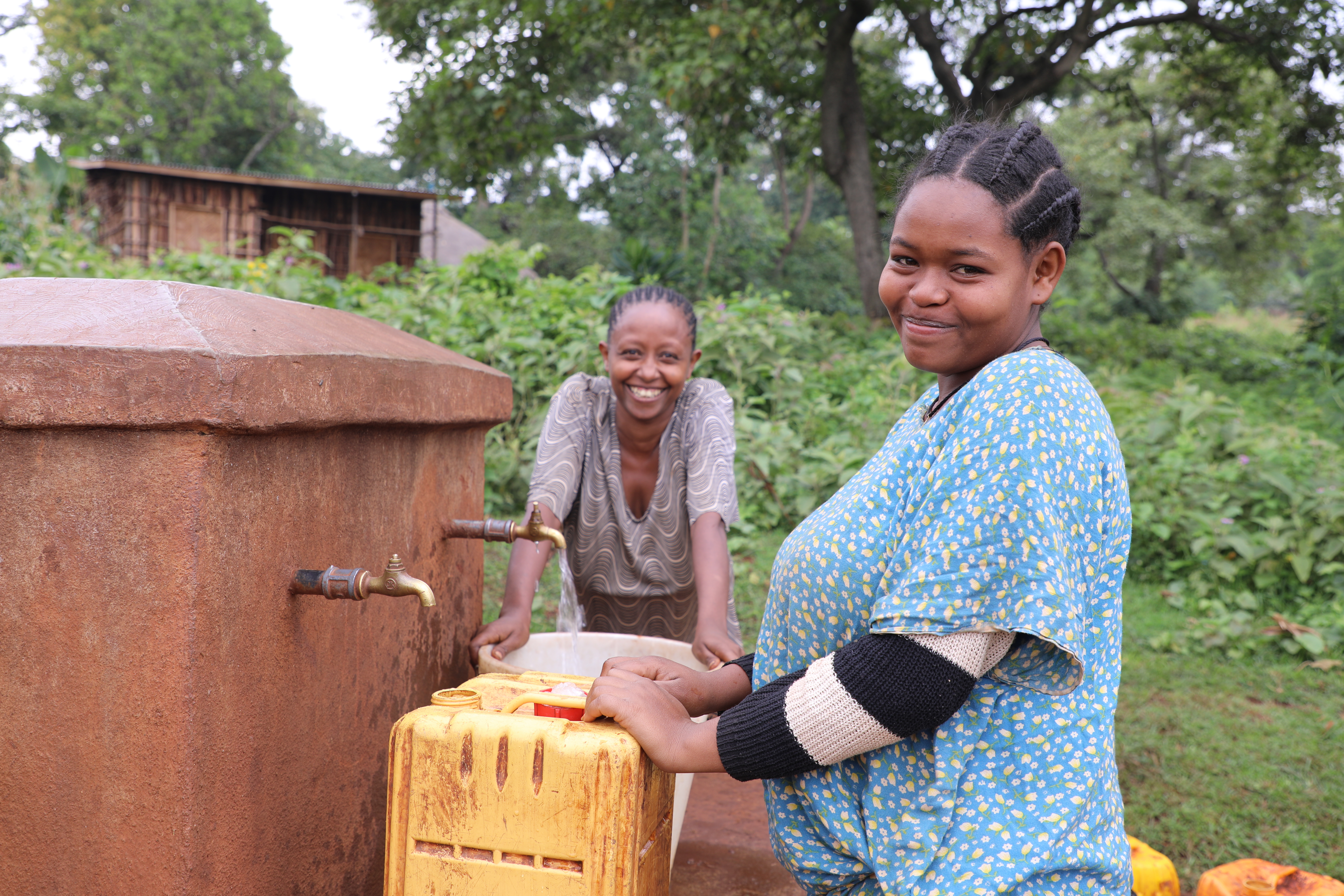 Dos colegialas de Etiopía llenando tinas de agua para sus hogares, mientras sonríen y miran a la cámara