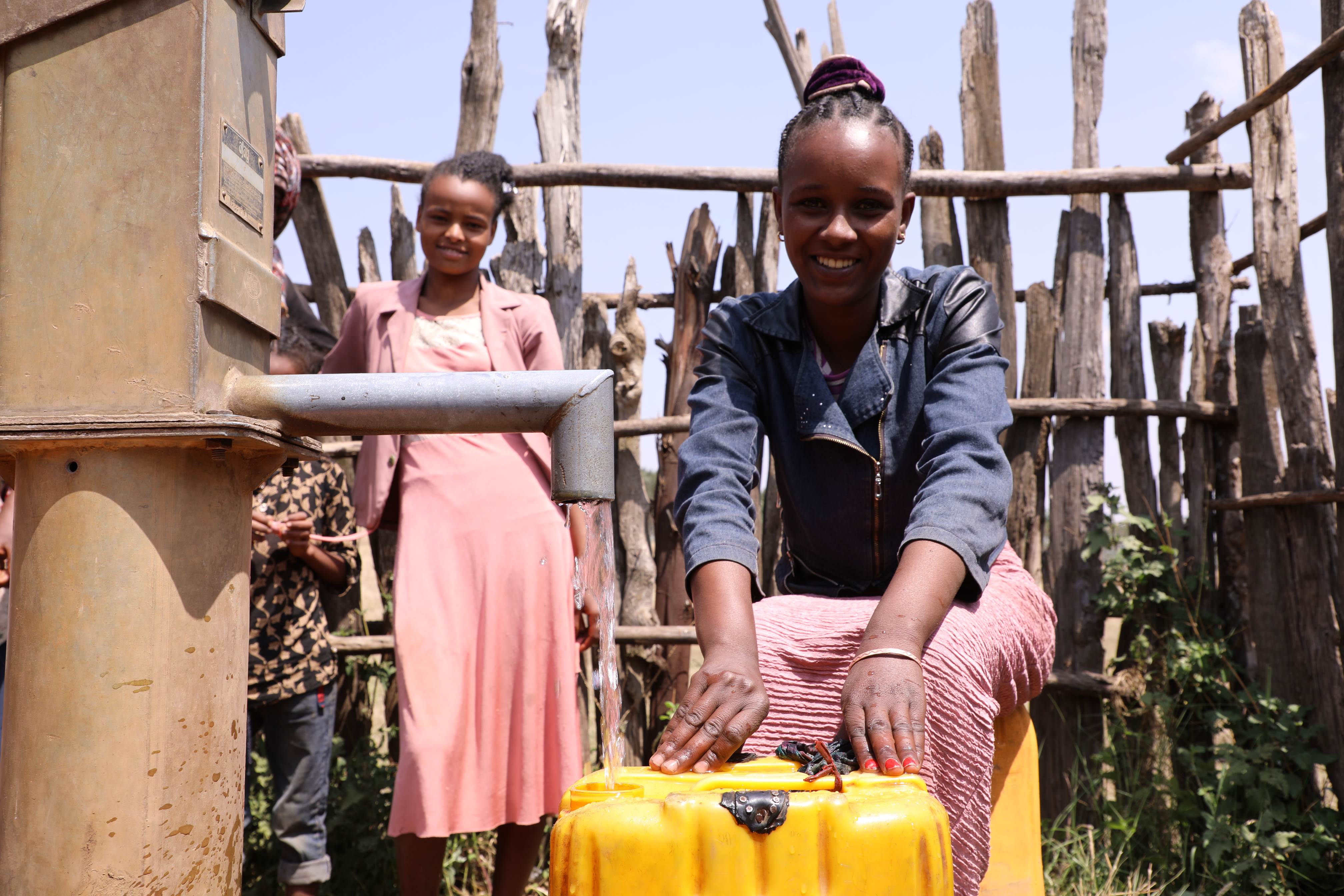 Una niña etíope vierte agua del grifo público en un cubo amarillo para llevársela a casa