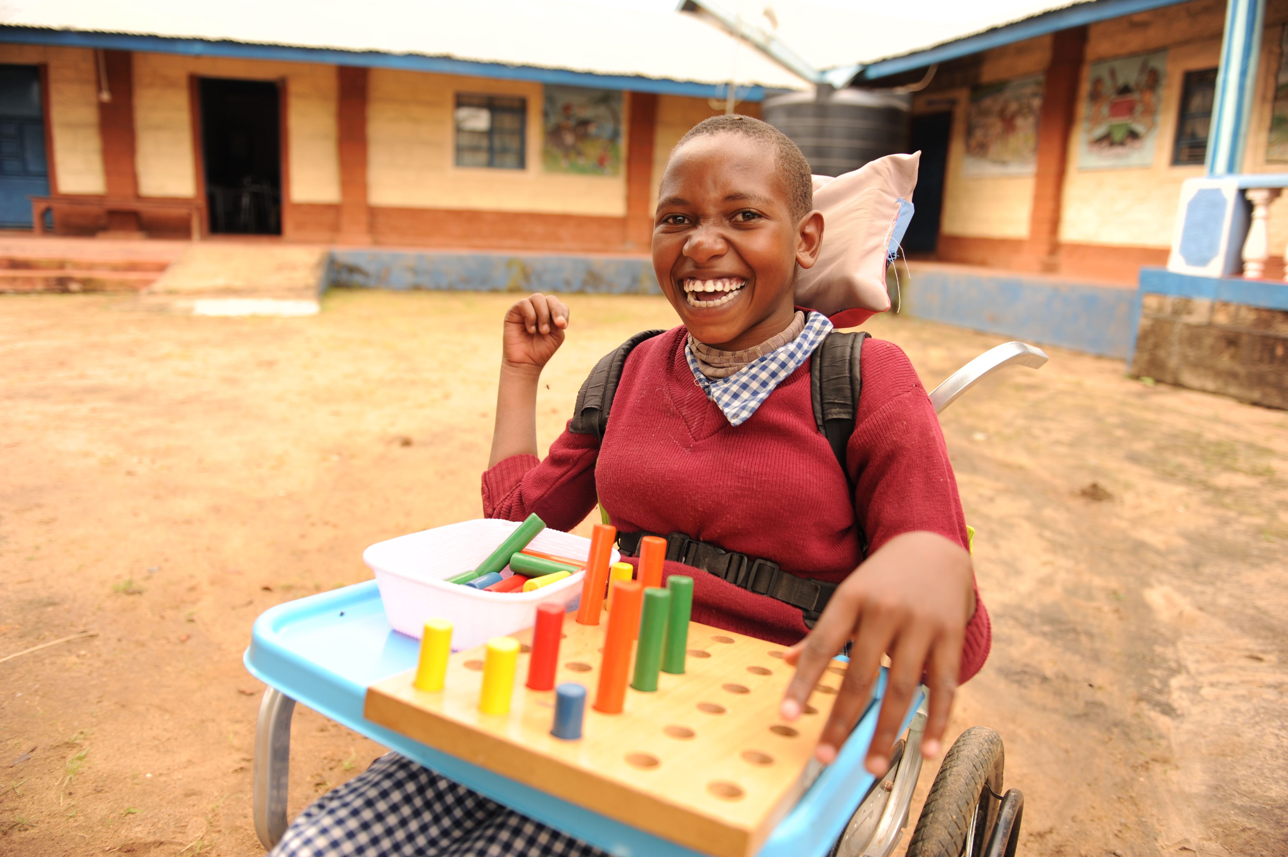 Niña de Kenia sonriendo sentada en su silla de ruedas y jugando con bloques