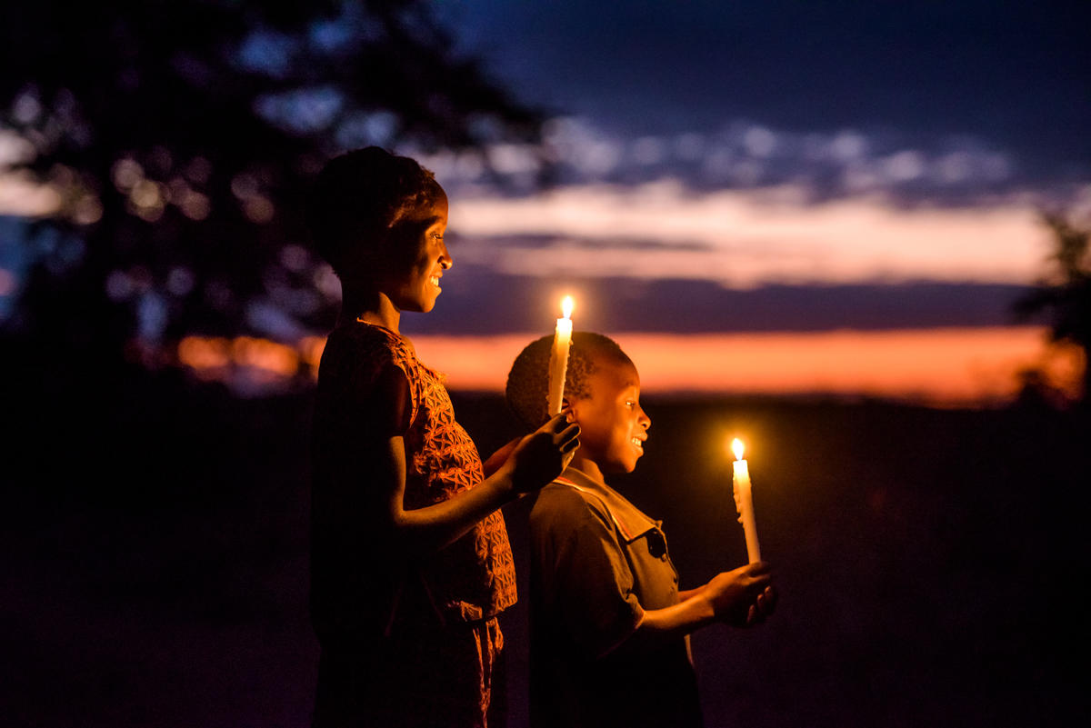 Niños en Zambia sonríen, sosteniendo velas afuera con una puesta de sol como telón de fondo