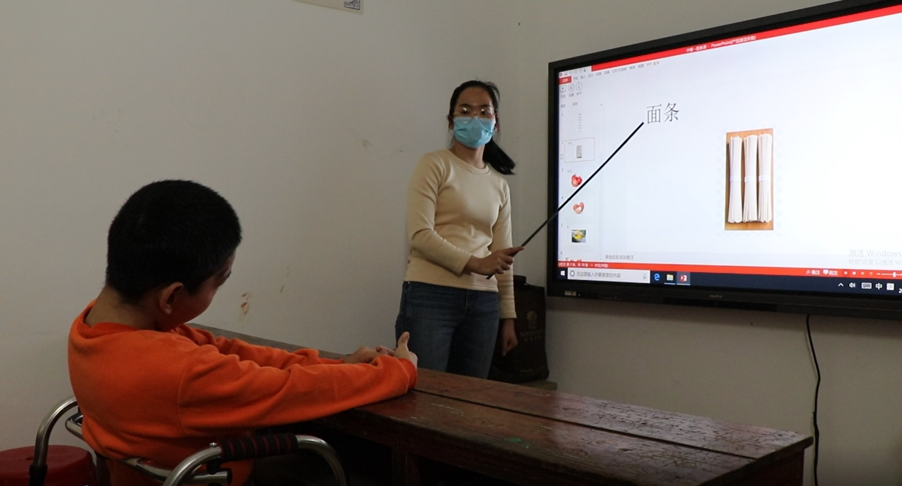 Woman wearing a facemask teaching a child on a projected whiteboard in a classroom in China