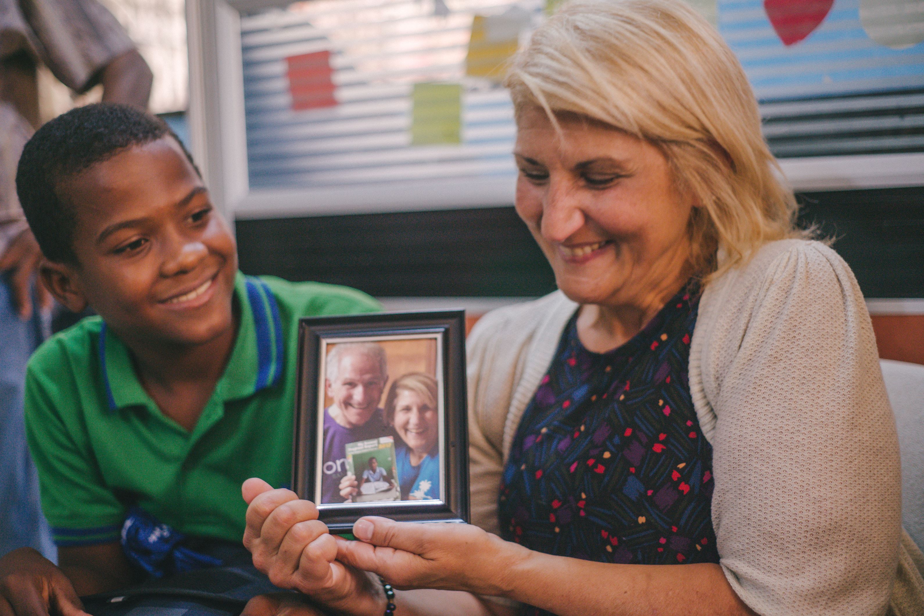 Niño se encuentra con su madrina en República Dominicana, y ella sostiene la foto de ella y su esposo el cual él aprecia