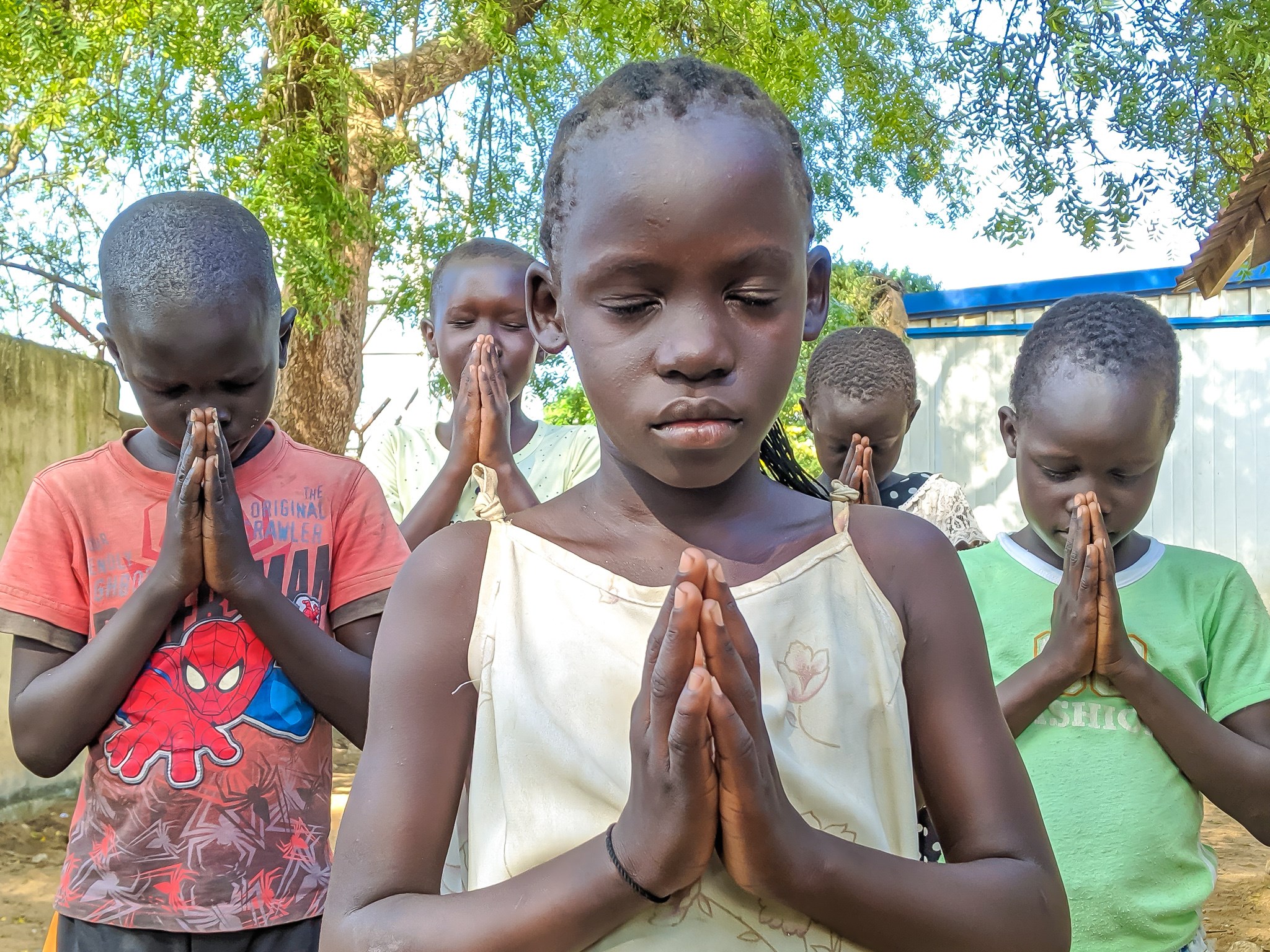 Grupo de niños en Sudán con los ojos cerrados rezando