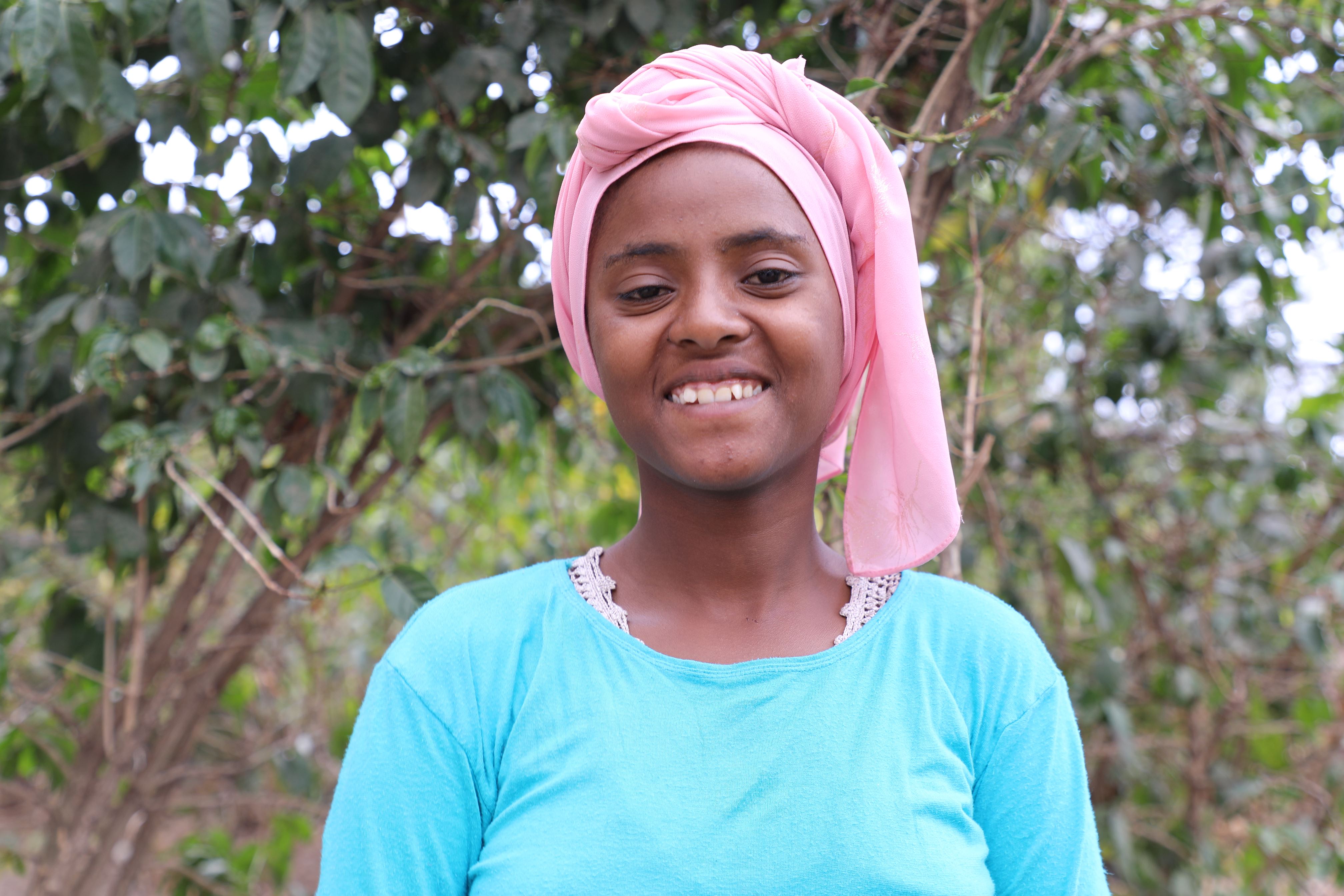 Chica de Etiopía de pie frente a un árbol, mirando a la cámara y sonriendo
