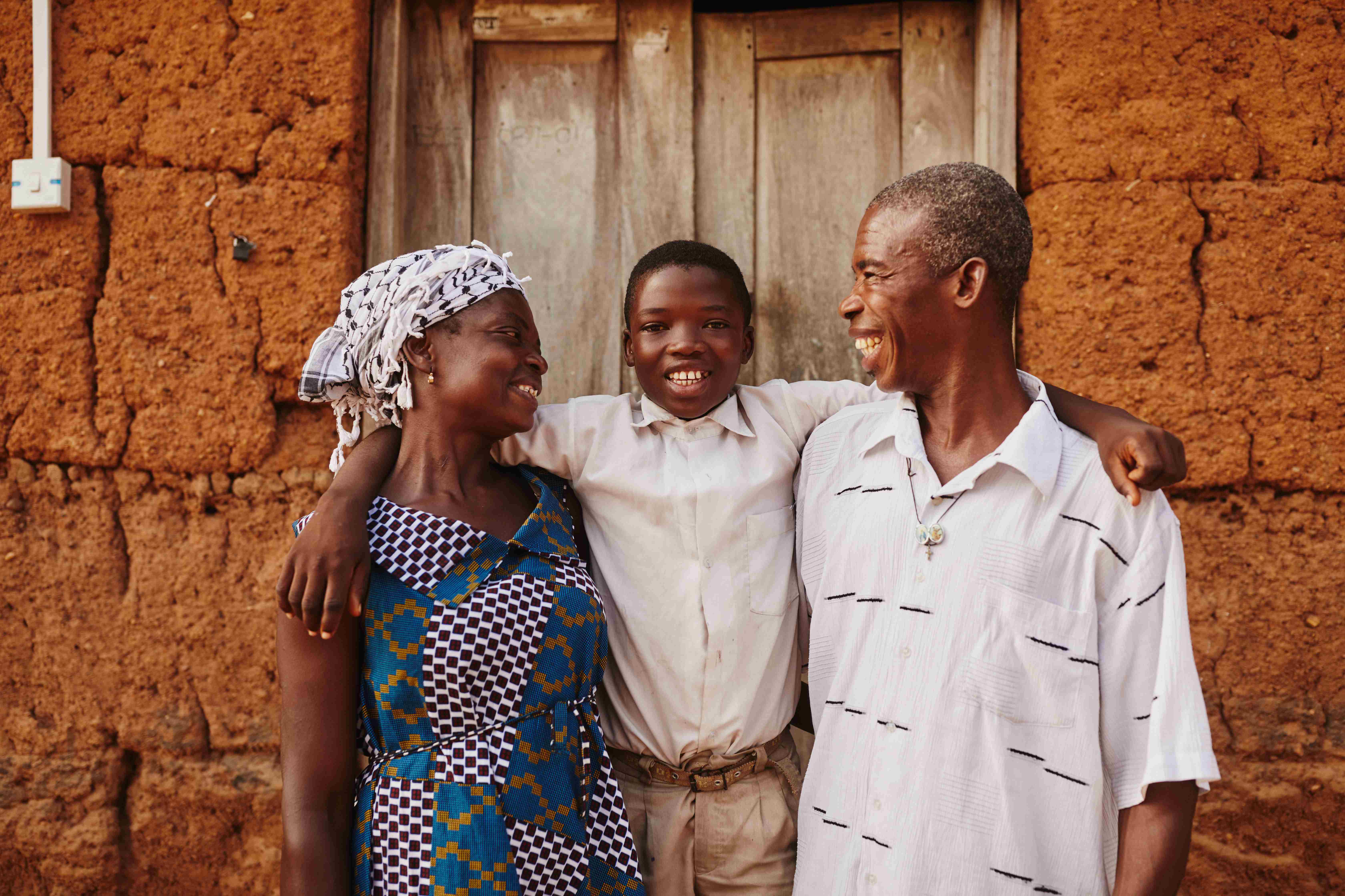 Un niño de Ghana entre sus padres, que lo abrazan y le sonríen