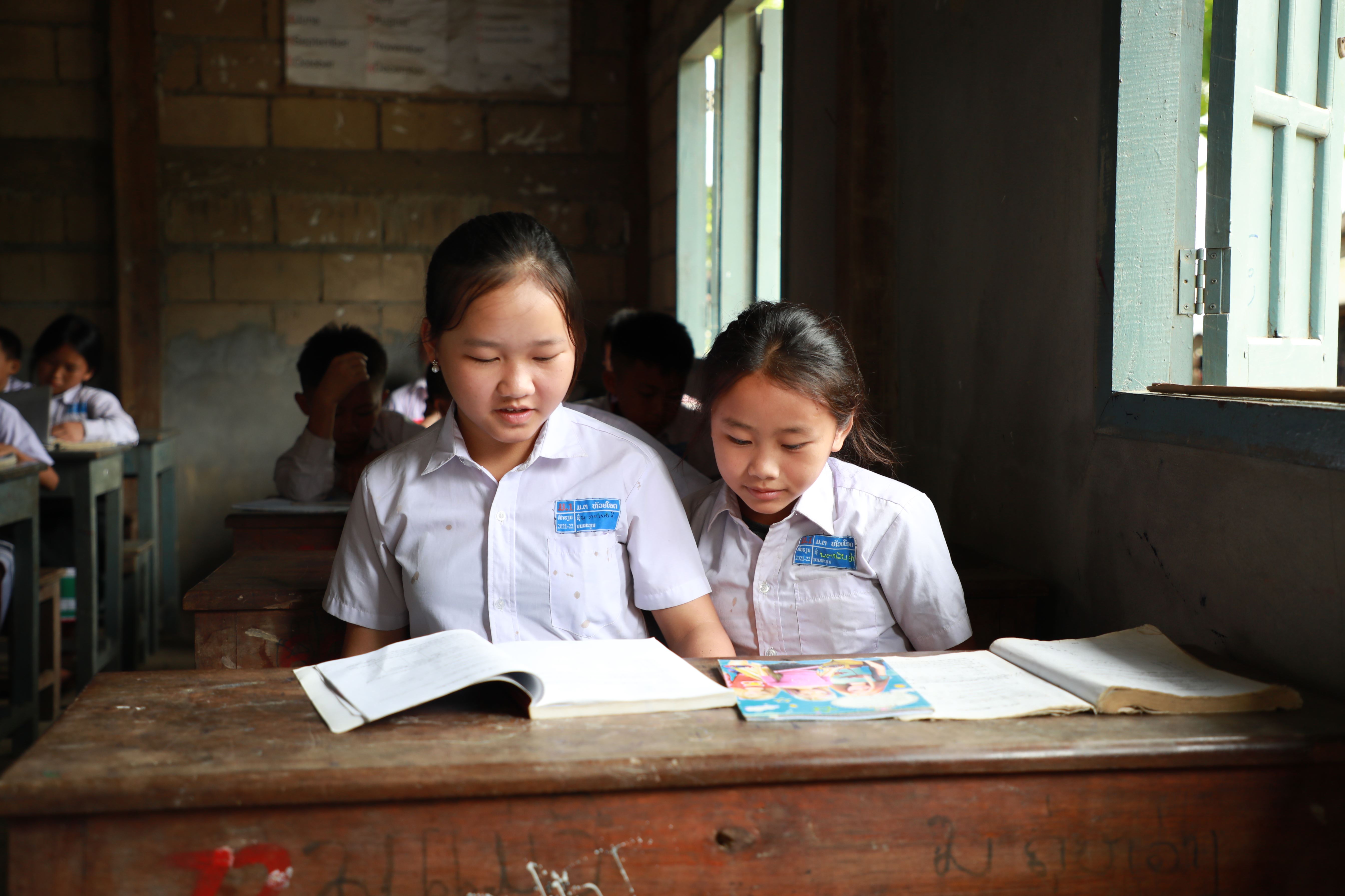 Dos escolares de Laos sentadas en un pupitre y leyendo un libro de texto