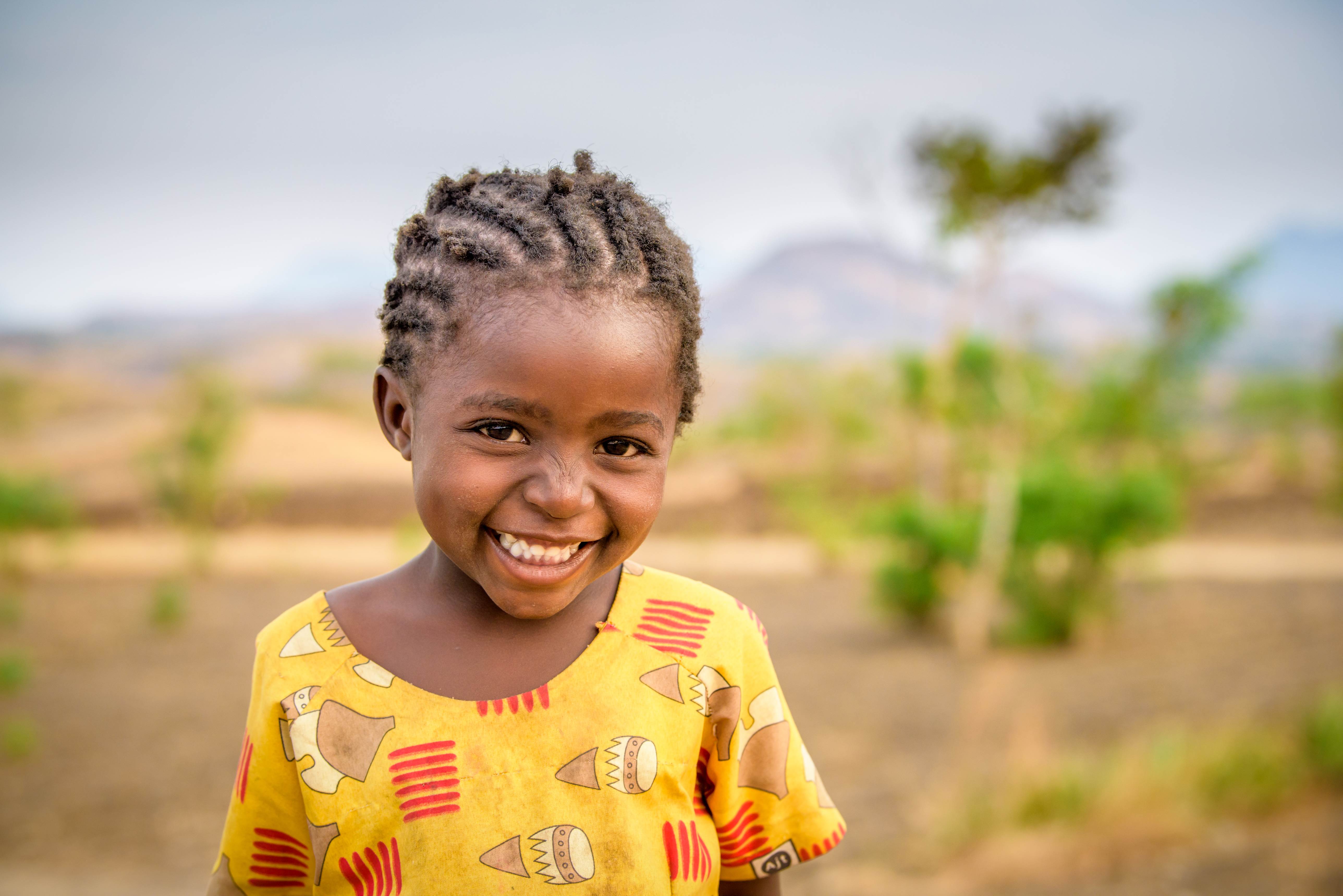 Niña apadrinada de 4 años de Malawi sonríe a la cámara mientras se sienta afuera