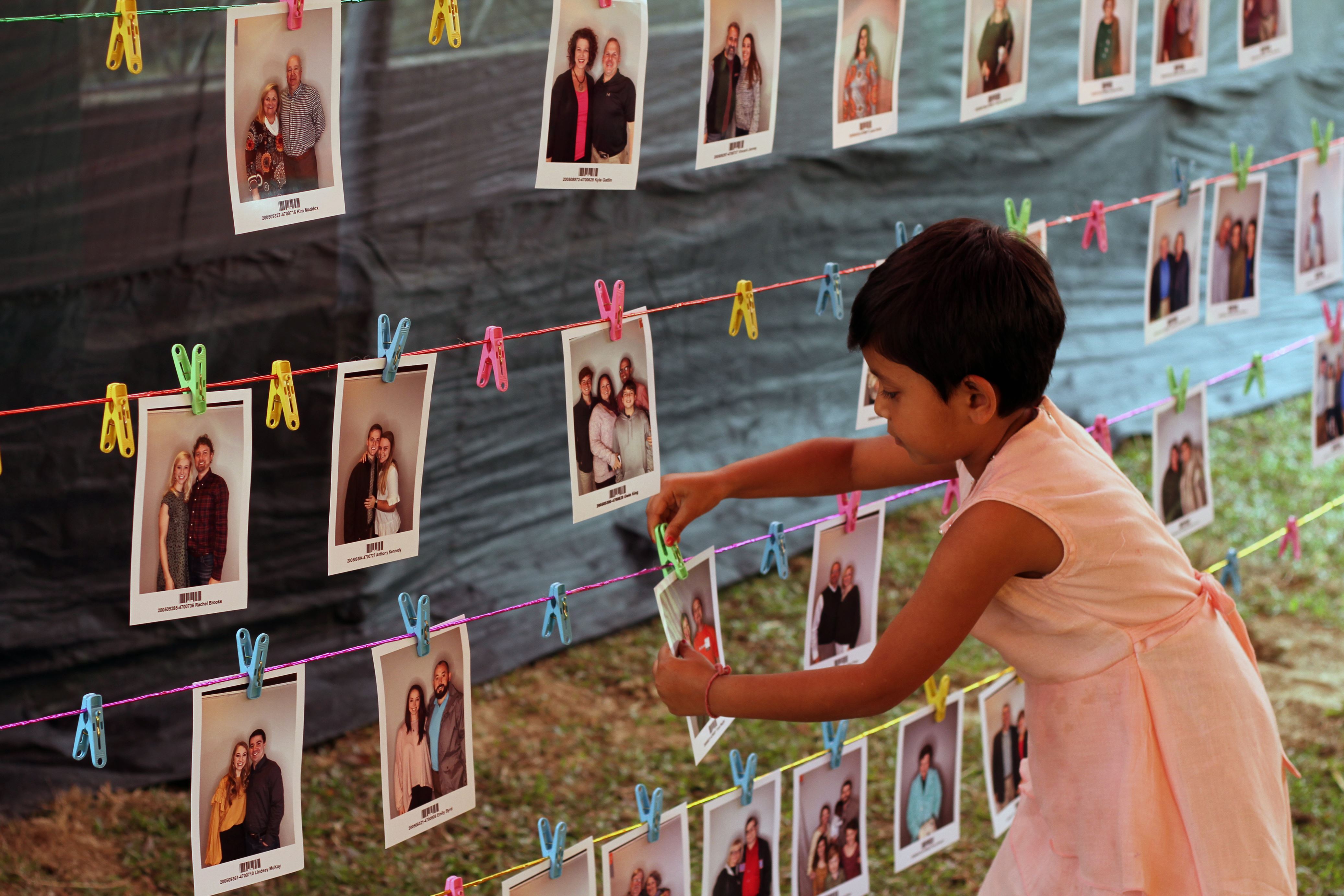 Chica en Bangladesh con un vestido rosa toma una foto de tres líneas de fotos de posibles patrocinadores que cuelgan de cables en una habitación
