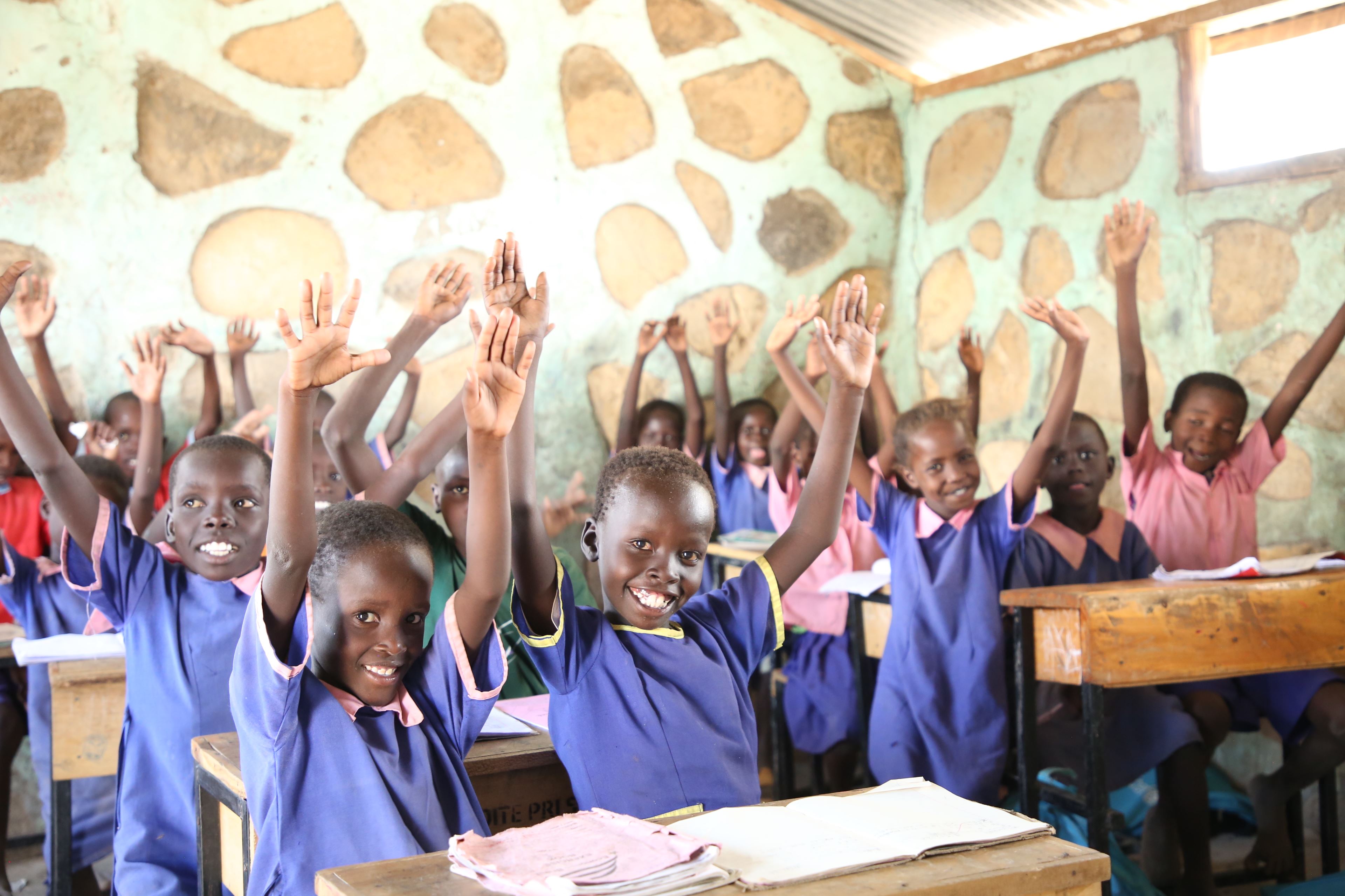 Classroom full of children raising their hands and smiling in Kenya