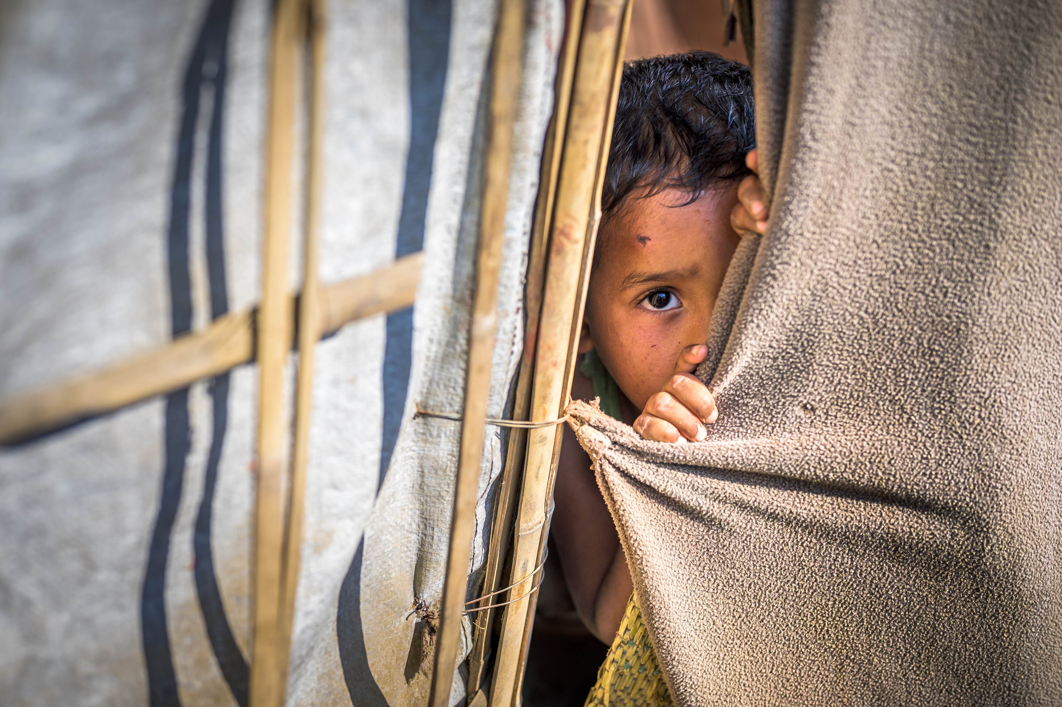 Un niño se asoma a través de una cortina en su refugio en Bangladesh