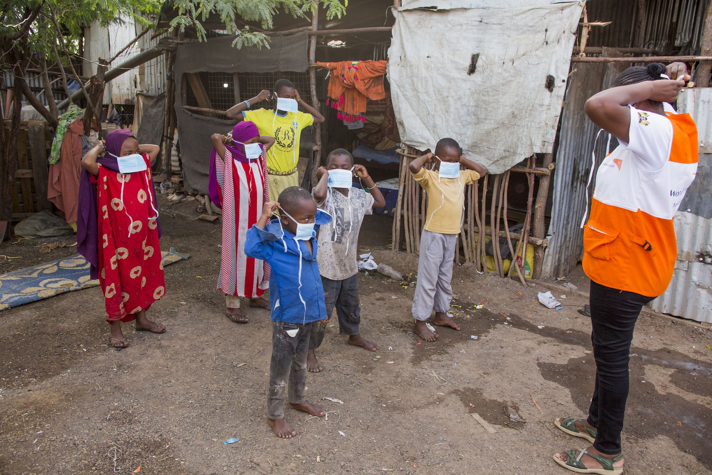 Un miembro del personal de World Vision frente a un grupo de niños enseñándoles como ponerse correctamente la mascarilla