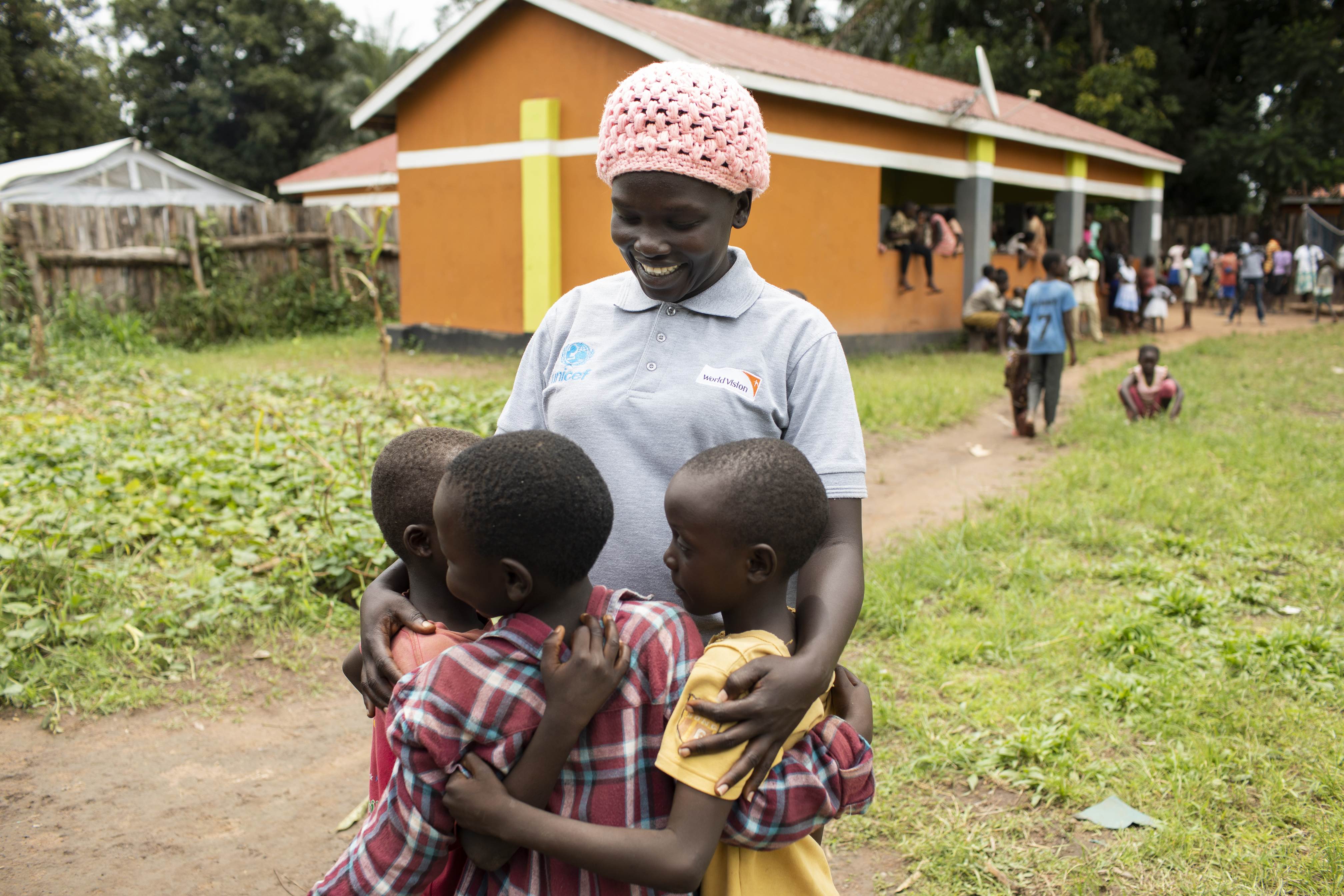Voluntarios de World Vision en Sudán del Sur abrazando a tres niños frente a una escuela recién construida