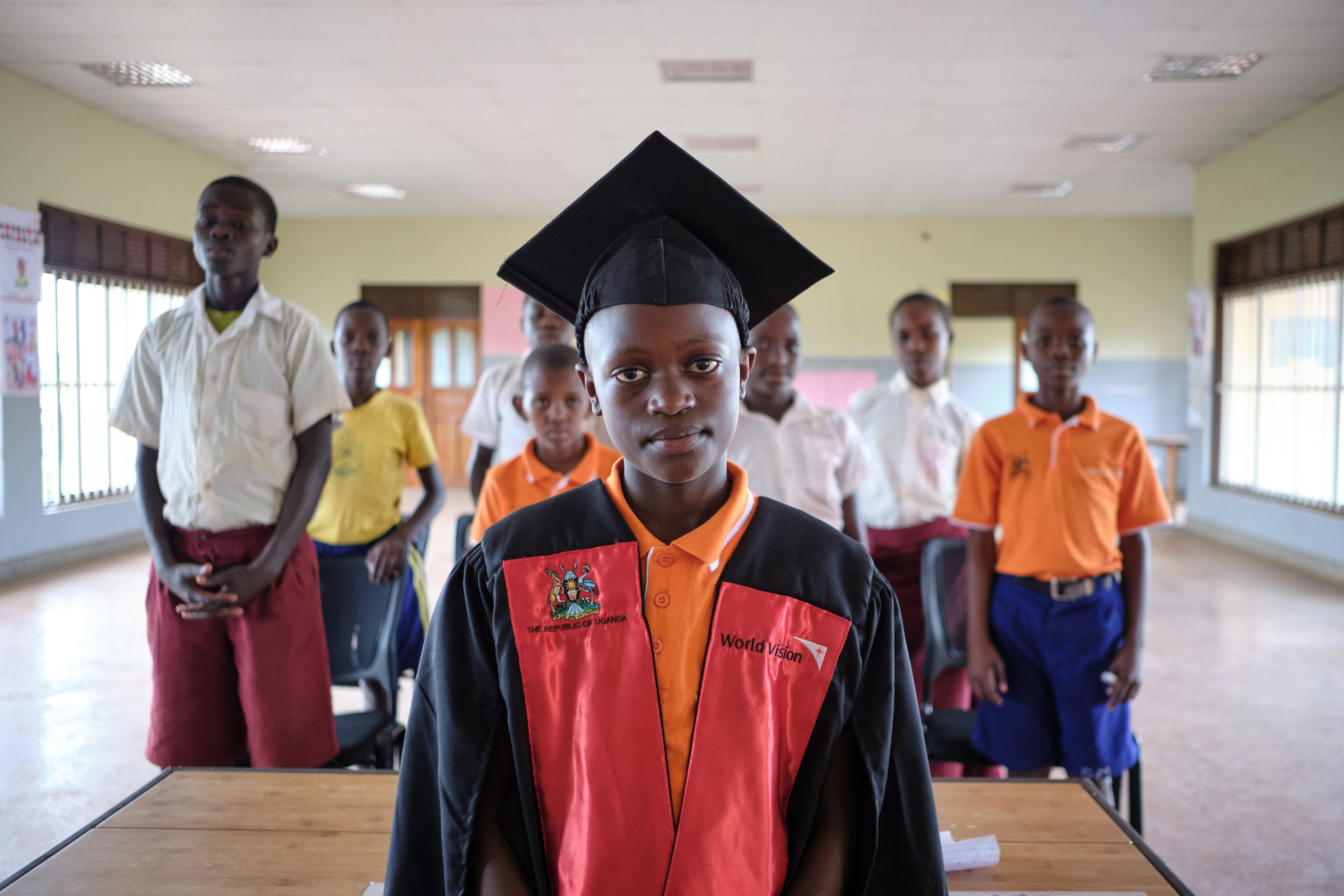 Niño ugandés de pie en una clase, detrás de él se ve a otros estudiantes.