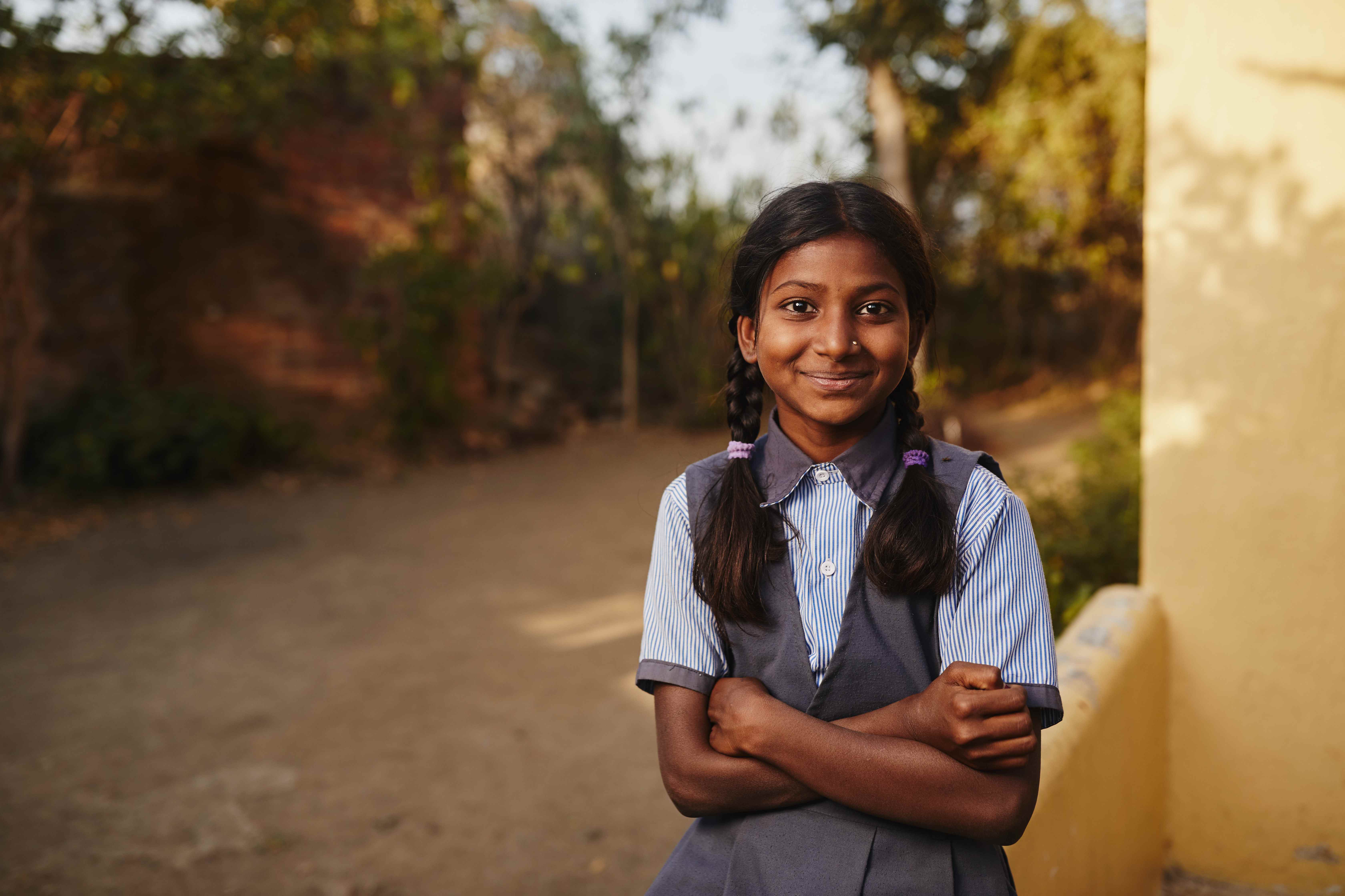 Escolar de la India con los brazos cruzados sonriendo y mirando a la cámara